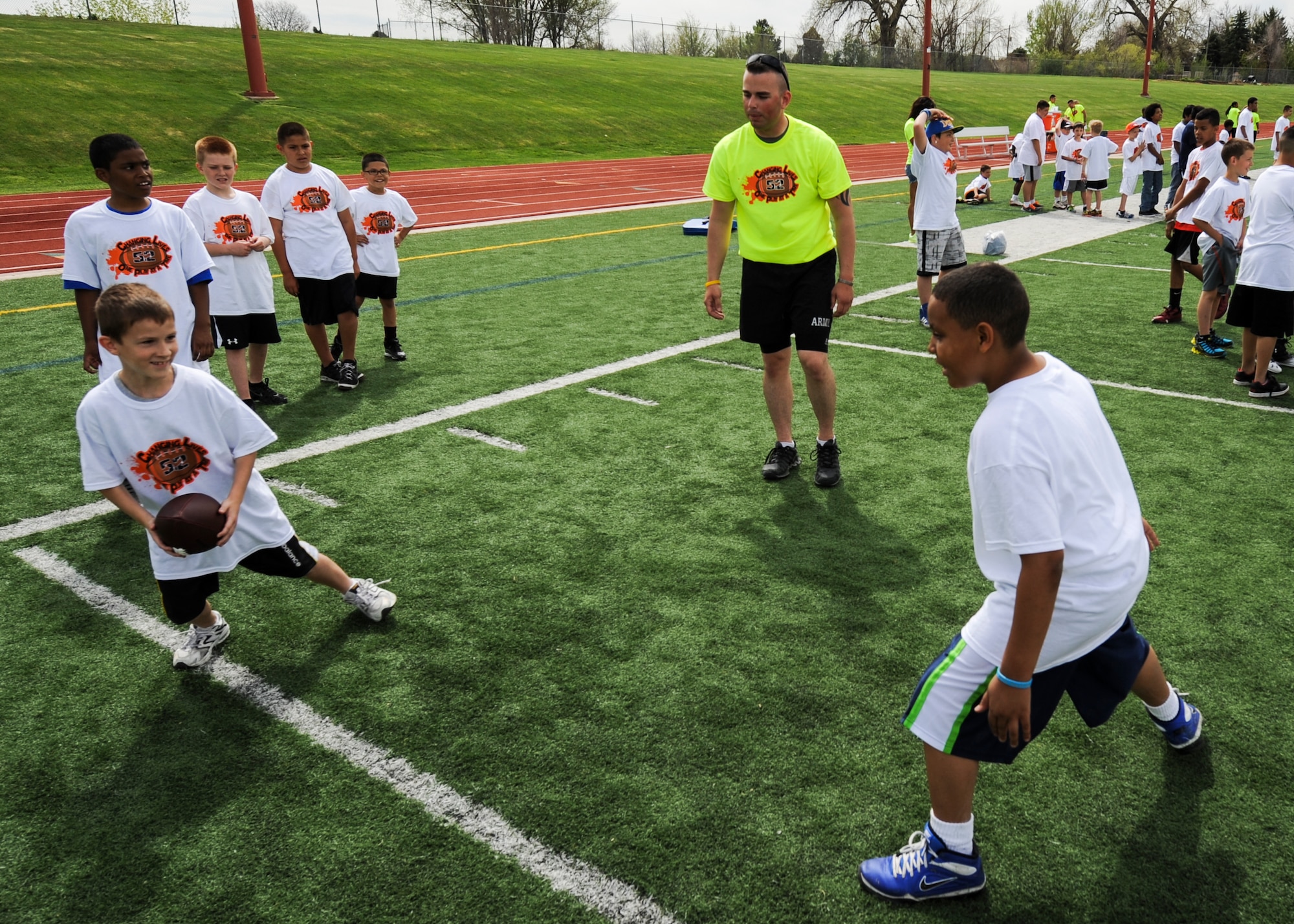 Douglas Blisardengler, in yellow, instructs children during a drill at the 16Ways football camp May 18, 2013, at the Aurora Public Stadium, Aurora, Colo. Blisardengler, an Army sergeant with the 743rd Military Intelligence Battalion, was one of about 30 volunteers from Buckley Air Force Base who participated in teaching more than 200 children between the ages of 8 to 14 the fundamentals of football along with the importance of teamwork and putting a stop to bullying. (U.S. Air Force photo by Staff Sgt. Christopher Gross/Released)
