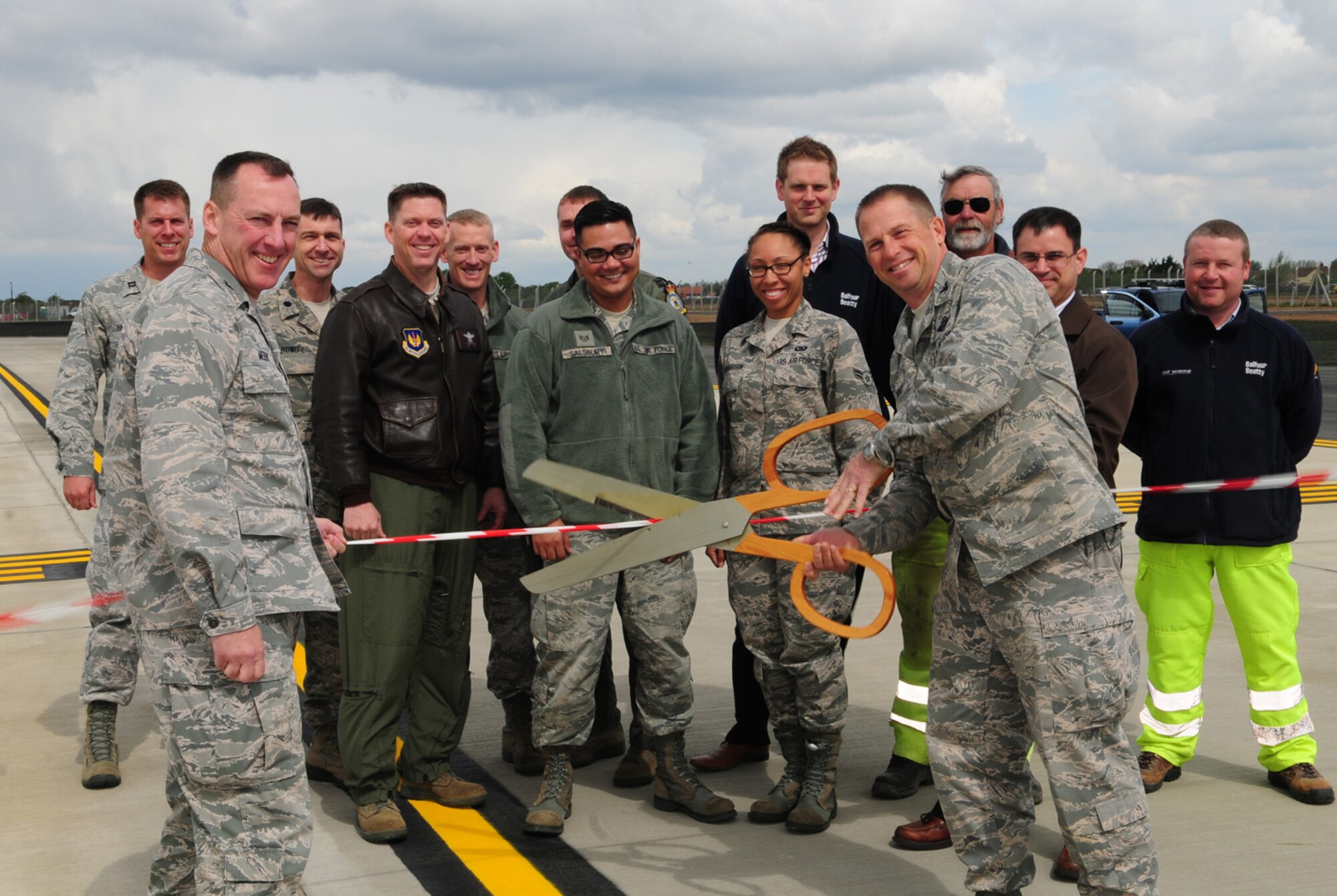 From front right, Col. Kyle Voigt, 100th Air Refueling Wing vice commander, cuts the ribbon marking the official opening of Taxiway Echo with Col. Daniel Merry, 100th Mission Support Group commander, May 23, 2013, on RAF Mildenhall, England. Taxiway Echo, an extension to Taxiway Alpha, will provide direct access for heavy aircraft to launch from the overrun and allow for swifter takeoffs.  The fiscal 2011 project cost $14.8 million and construction started June 2012. (U.S. Air Force photo by Karen Abeyasekere/Released)