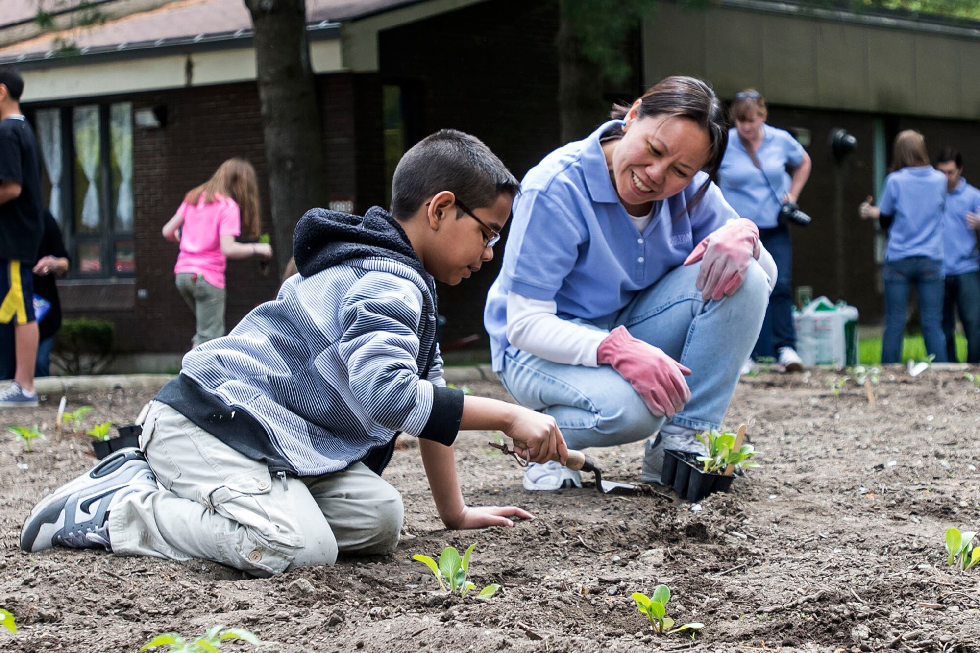 HANSCOM AIR FORCE BASE, Mass. – Kamrin Saladine (left) and Lan Dennie, a U.S. Family Health Plan volunteer, work together planting flowers, herbs and vegetables in the community garden near the Youth Center May 15. Children from the Youth Center were joined by volunteers to plant the community garden for children to enjoy this summer. Children and volunteers began the project with a barbecue that was prepared by Youth Center staff and USFHP volunteers. (U.S. Air Force photo by Walter Santos) 