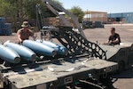 Staff Sgt. Scott Thompson, munitions technician, drives a MJ-1B bomb lift to load BDU-50 inert bombs to a trailer for assembly and transport to the flight line. Master Sgt. Jim Stenger, assistant munitions supervisor, guides the bombs during transport to the trailer. This bomb lift, and others like it, is maintained by the wing's aerospace ground equipment shop.
