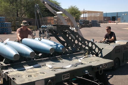 Staff Sgt. Scott Thompson, munitions technician, drives a MJ-1B bomb lift to load BDU-50 inert bombs to a trailer for assembly and transport to the flight line. Master Sgt. Jim Stenger, assistant munitions supervisor, guides the bombs during transport to the trailer. This bomb lift, and others like it, is maintained by the wing's aerospace ground equipment shop.