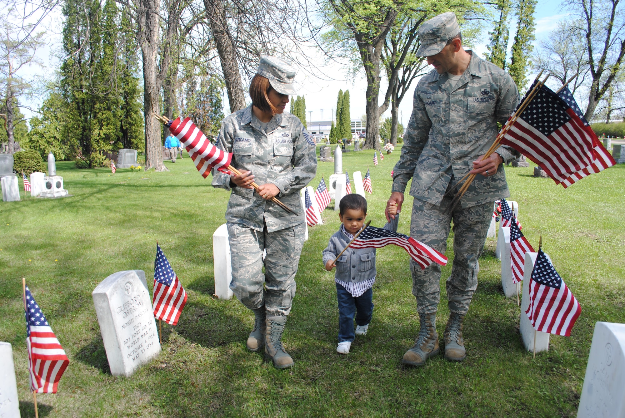 Master Sgt. Claudia Carcamo and Chief Master Sgt. Marlon Carcamo guide their 2-year-old son, Javier, down a row of white tombstones adorned with small U.S. flags on May 24, 2013. The Carcamos were one of several families from Grand Forks Air Force Base, N.D., to volunteer to place flags on the tombs of fallen service members at Calvary Cemetery in Grand Forks, N.D., in honor of this year’s Memorial Day. (U.S. Air Force photo/Staff Sgt. Luis Loza Gutierrez)
