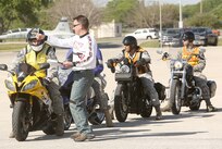 Air Force Master Sgt. John Carter (standing), 937th Training Wing, instructs Air Force Staff Sgt. David Wilson of the 668th Alteration and Installation Squadron before he participates in a motorcycle safety rally. (Air Force photo by Robbin Cresswell, JBSA-Lackland Public Affairs)