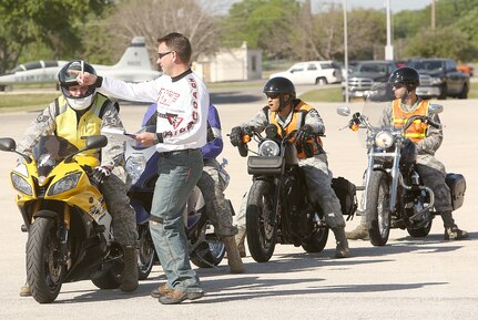 Air Force Master Sgt. John Carter (standing), 937th Training Wing, instructs Air Force Staff Sgt. David Wilson of the 668th Alteration and Installation Squadron before he participates in a motorcycle safety rally. (Air Force photo by Robbin Cresswell, JBSA-Lackland Public Affairs)