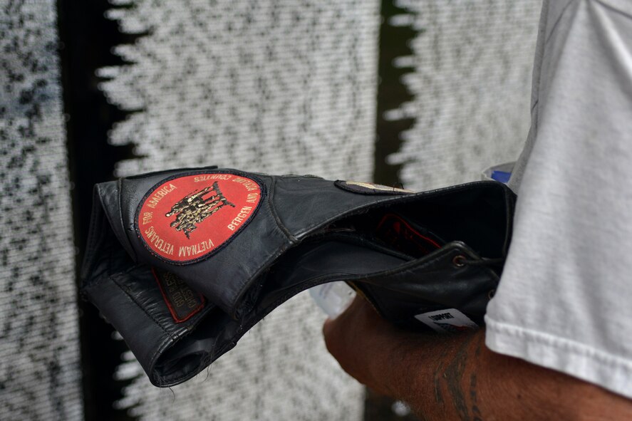 The veteran patch of George Pilioglos is held in the foreground in front of the Vietnam Memorial Wall as he takes a moment to remember fallen friends, Sumter, S.C., May 23, 2013. The traveling memorial made its only stop in S.C., at Sumter’s Swan Lake. The wall stands six feet tall at the center and covers almost 300 feet from end to end. (U.S. Air Force photo by Airman 1st Class Ashley L. Gardner/Released)
