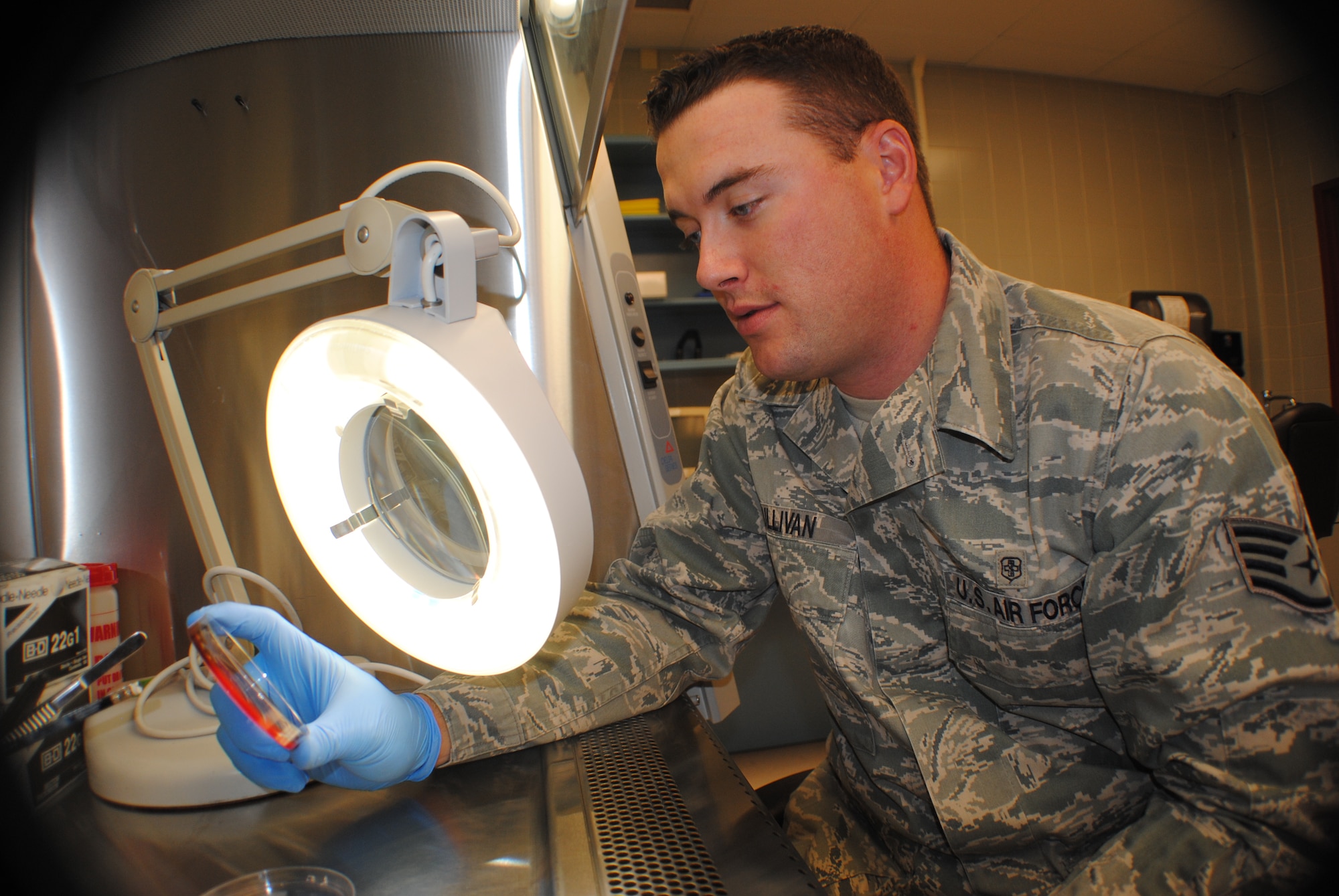 Staff Sgt. Thomas C. Sullivan Jr., 319th Medical Support Squadron laboratory technician, checks the growth progress of bacteria cultures using a magnifying lamp inside a bio-safety examining cabinet May 22, 2013, at Grand Forks Air Force Base, N.D. Air Force medical lab technicians go through a four month-long training course at Sheppard AFB, Texas, for the first phase of their technical training. (U.S. Air Force photo/Staff Sgt. Luis Loza Gutierrez)