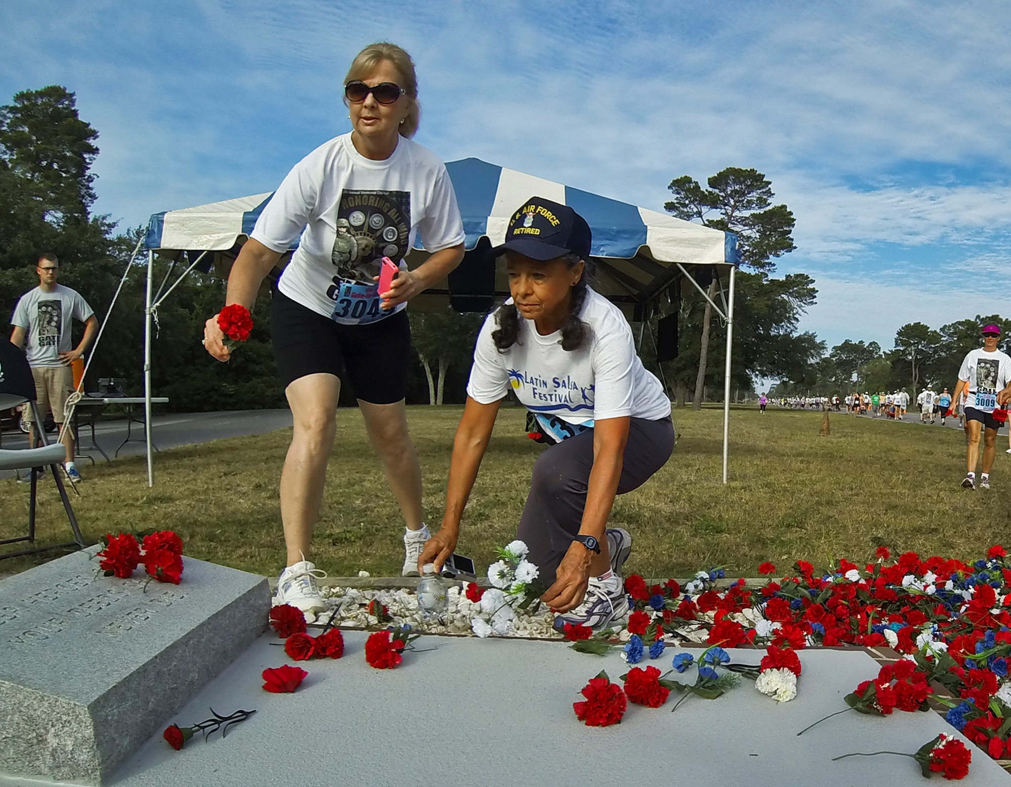 Joni LaFlamme (left) stops to honor the veterans by placing a flower on the memorial during the 28th annual Gate-to-Gate Run May 27 at Eglin Air Force Base, Fla. More than 1,500 people participated in the Memorial Day race.  Many of the runners paid their respects by dropping off flowers in front of the All Wars Memorial as they raced by.  (U.S. Air Force photo/Samuel King Jr.)