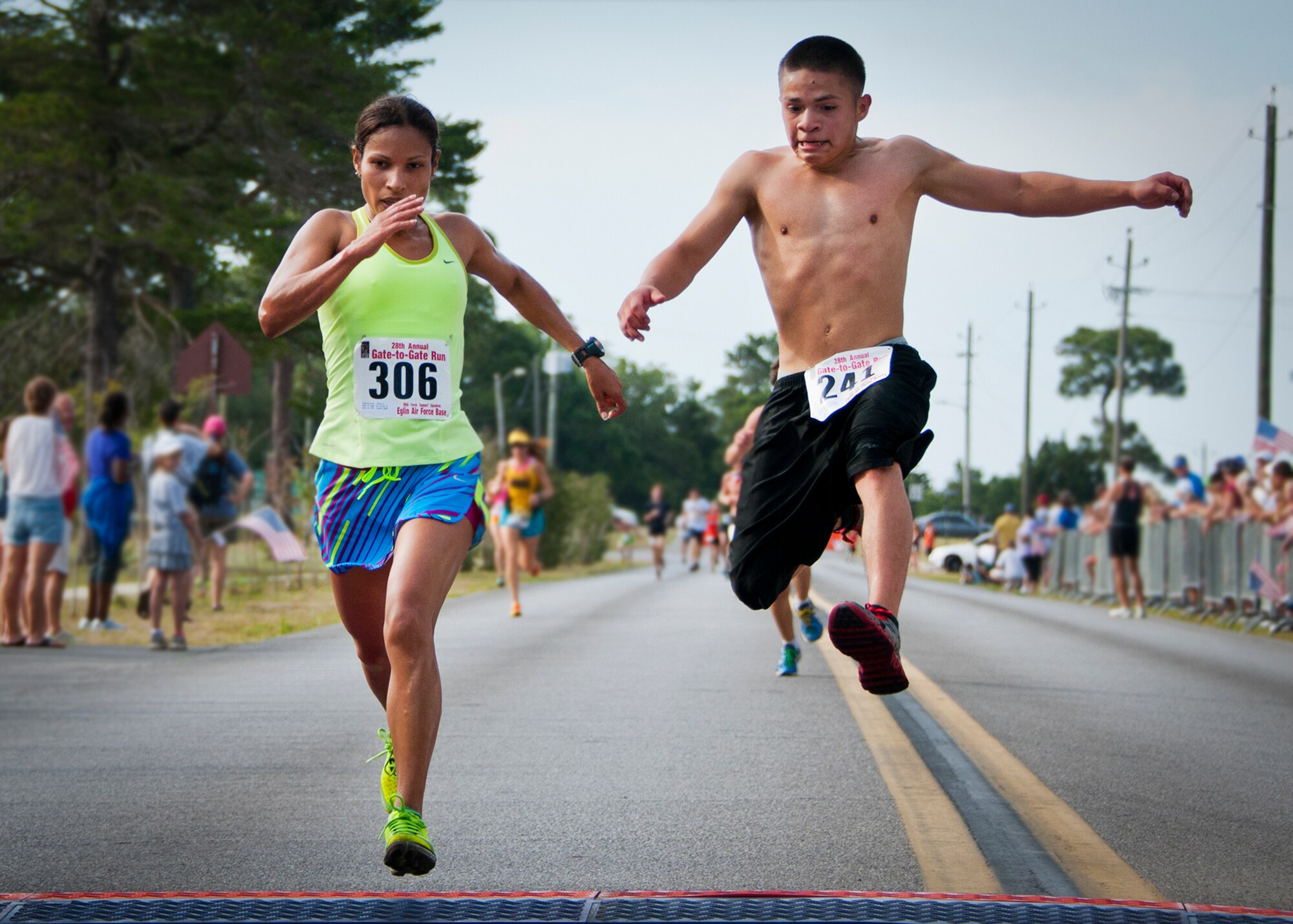 Thais Gutierrez and Matthew Espinoza leap to try and cross the finish line first during the 28th annual Gate-to-Gate Run May 27 at Eglin Air Force Base, Fla. More than 1,500 people participated in the Memorial Day race.  Many of the runners paid their respects by dropping off flowers in front of the All Wars Memorial as they raced by.  (U.S. Air Force photo/Samuel King Jr.)
