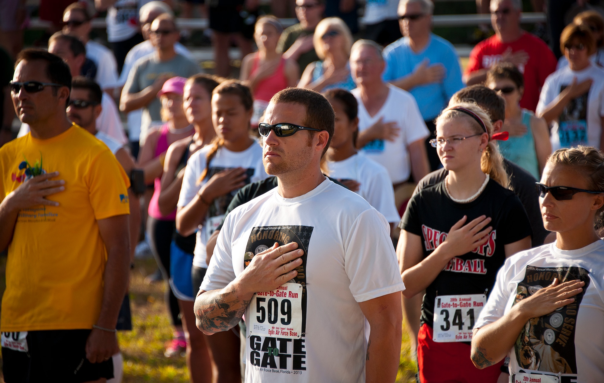 Everyone in the crowd, including Dathan Nordheim (middle), held their hand to their heart or stood at attention during the National Anthem at the 28th annual Gate to Gate Run May 27 at Eglin Air Force Base, Fla.  More than 1,500 people participated in the Memorial Day race.  Many of the runners paid their respects by dropping off flowers in front of the All Wars Memorial as they raced by.  (U.S. Air Force photo/Samuel King Jr.)