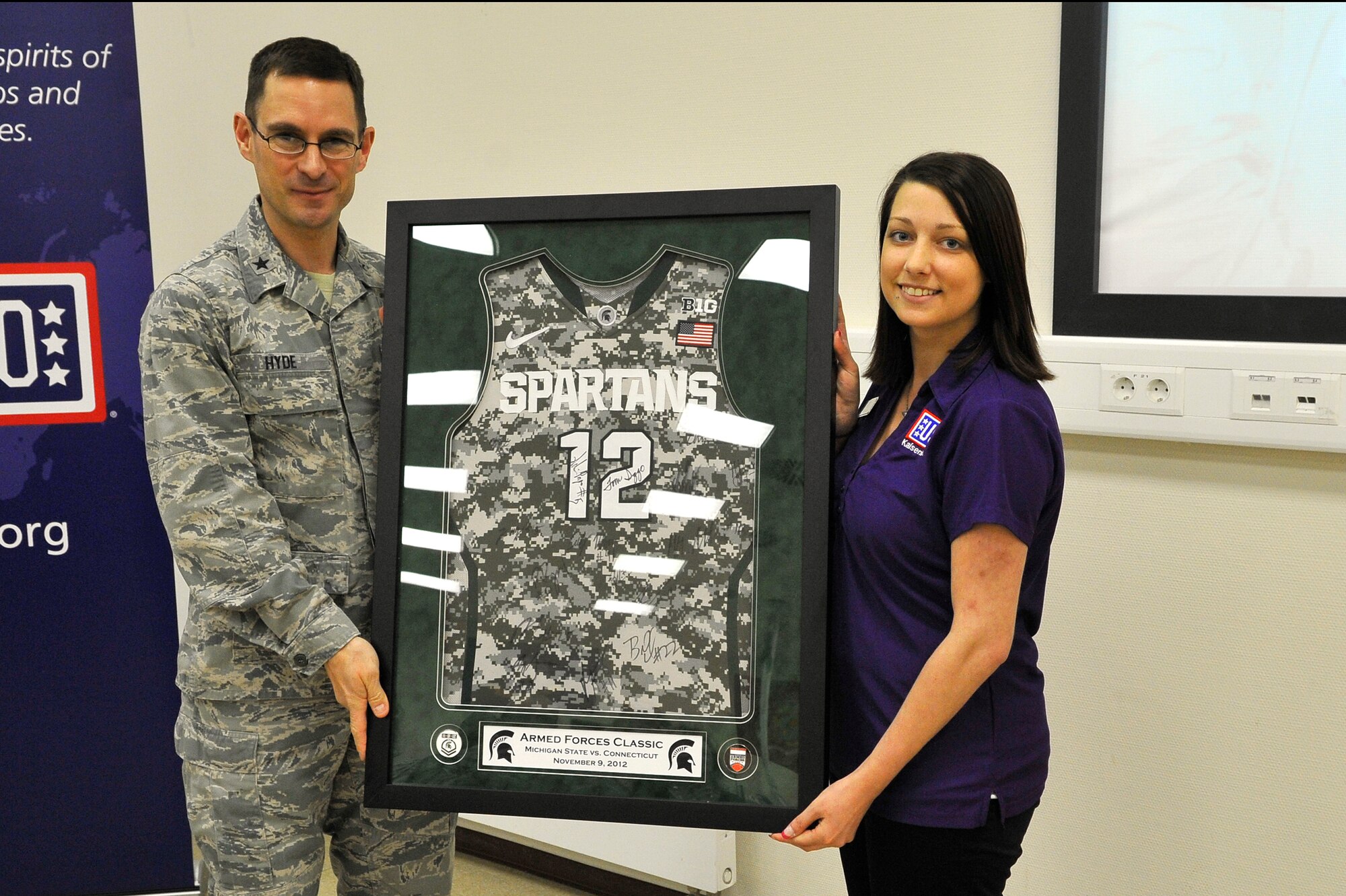 Brig. Gen. C.K. Hyde, 86th Airlift Wing commander presents a signed Michigan State Spartans basketball jersey to Jessica Maraca, Contingency Aeromedical Staging Facility USO center manager during the 10th Anniversary of the CASF USO celebration, May 22, 2013, Ramstein Air Base, Germany. The CASF USO offers a home away from home for wounded service members in transit from combat zones to the U.S. (U.S. Air Force photo/Airman 1st Class Trevor Rhynes)