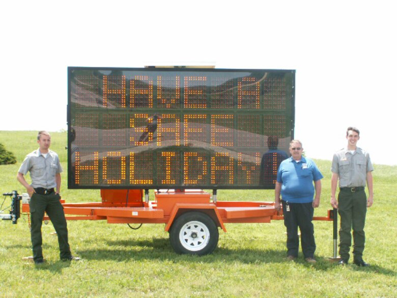Water safety rangers Travis Sipe (Melvern Lake) and Lance Caldwell (Pomona Lake) pose with Bryce Romine, the Osage County Emergency Management director, in front of a highway control sign promoting safety during the Memorial Day weekend. Photo by James D. Franz.