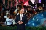 Retired Army Gen. Colin Powell stands at a microphone with concert players on a stage in the background.