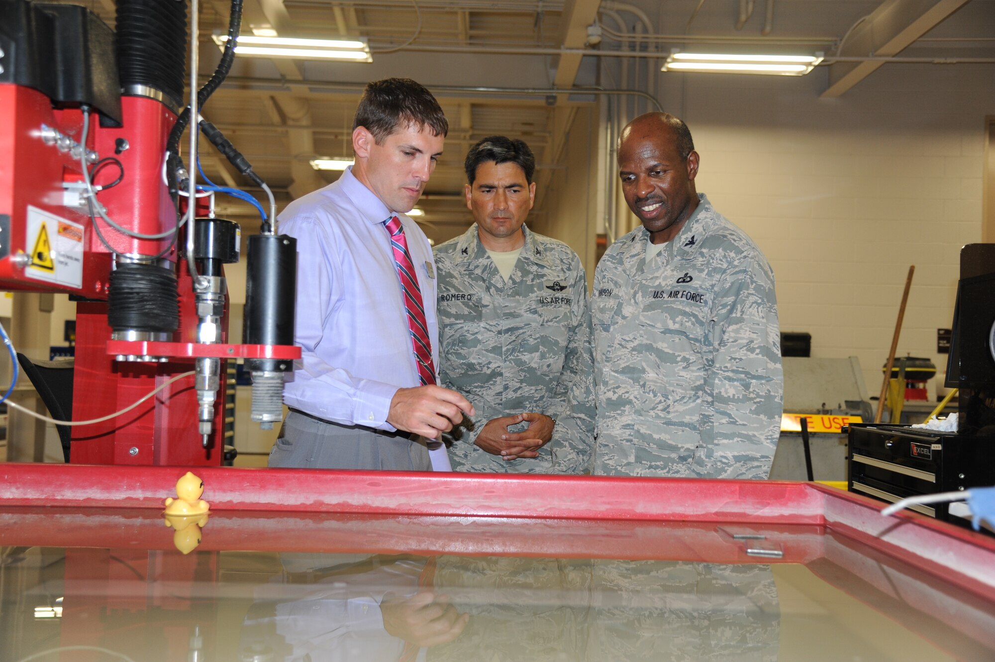 Tomme Lassabe, 81st Training Support Squadron, briefs Col. René Romero, 81st Training Wing vice commander, and Col. Malcolm “TJ” Johnson, 2nd Air Force vice commander, on the capabilities of a water jet cutting system which uses compressed water pressure along with an aggregate to penetrate various materials inside the Trainer Development Center during Johnson’s two-day immersion with the 81st Training Wing May 29, 2013, at Keesler Air Force Base, Miss.  (U.S. Air Force photo by Kemberly Groue)