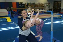 Ozlem Beckman, Joint Base San Antonio-Randolph Youth Center gymnastics coach, assists Jane Taylor with parallel bar exercises May 16 at the center. (U.S. Air Force photo by Joel Martinez/ Released)