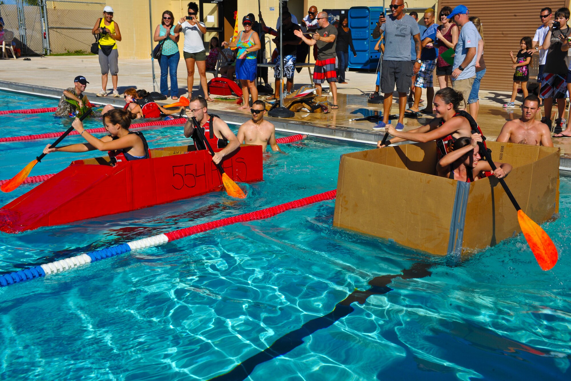 Members of the 554th  RED HORSE Squadron and the 36th Logistics Readiness Squadron Fuels Management Flight race their makeshift boats made with cardboard boxes and duct tape for a cardboard boat race May 24, 2013, on Andersen Air Force Base, Guam. The contest was part of the Memorial Day Bash, which also featured face painting, water buffalo riding, a dunk booth and a moon bounce obstacle course for the families. (U.S. Air Force photo by Senior Airman Robert Hicks/Released)
