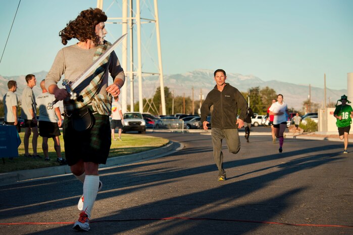 Wesley Morgan, 99th Air Base Wing executive officer, dressed as a Scottish Warrior, crosses the finish line during the Halloween 5 kilometer run at the Warrior Fitness Center Oct. 31, 2013, at Nellis Air Force Base, Nev. The best costume was judged by how much noise and enthusiasm the audience produced when each contestant was introduced. (U.S. Air Force photo by Airman 1st Class Timothy Young)