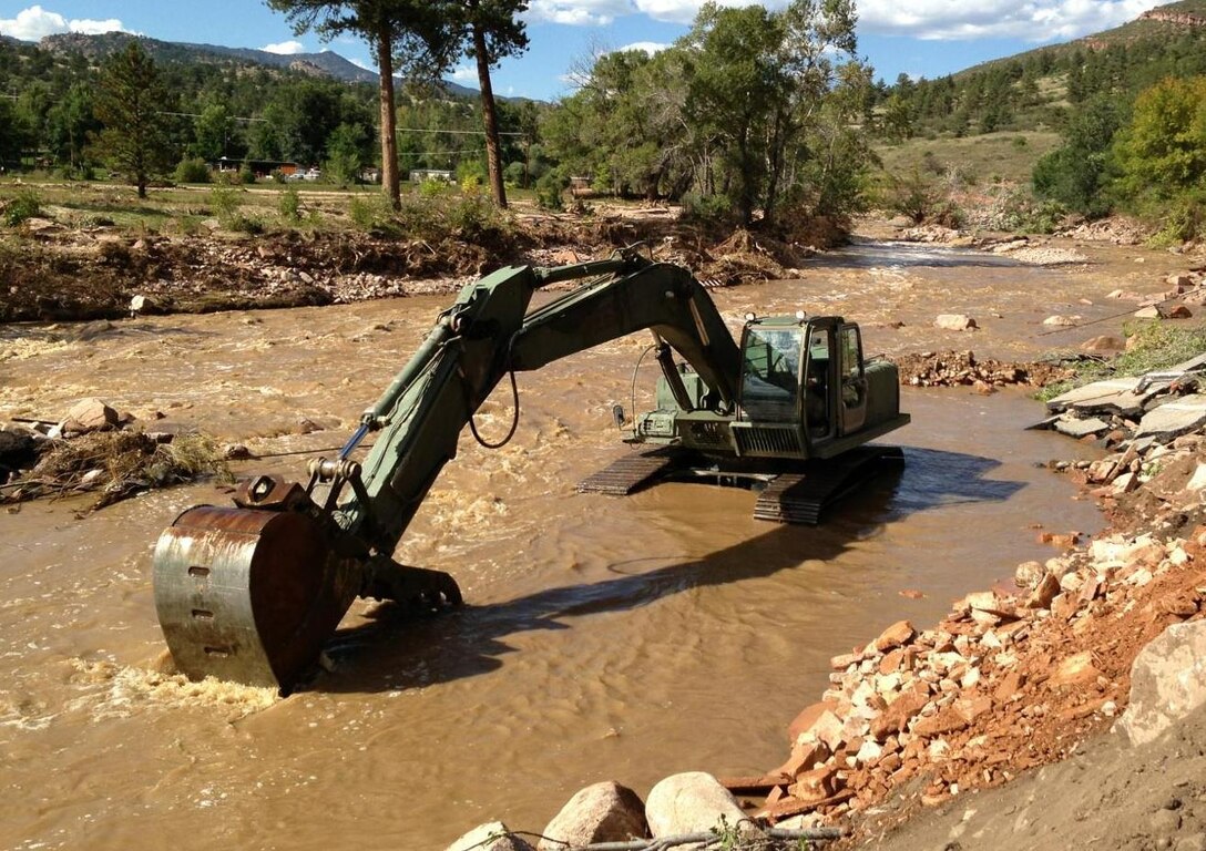 A military hydraulic excavator works to clear the remainder of a Colorado road after a flood washed it away. Many roads were destroyed during the Colorado flood leaving some Colorado residences stranded and forced to backpack in fuel and food to their homes. (File Photo by DART-W Public Affairs Office, 36th Infantry Division)