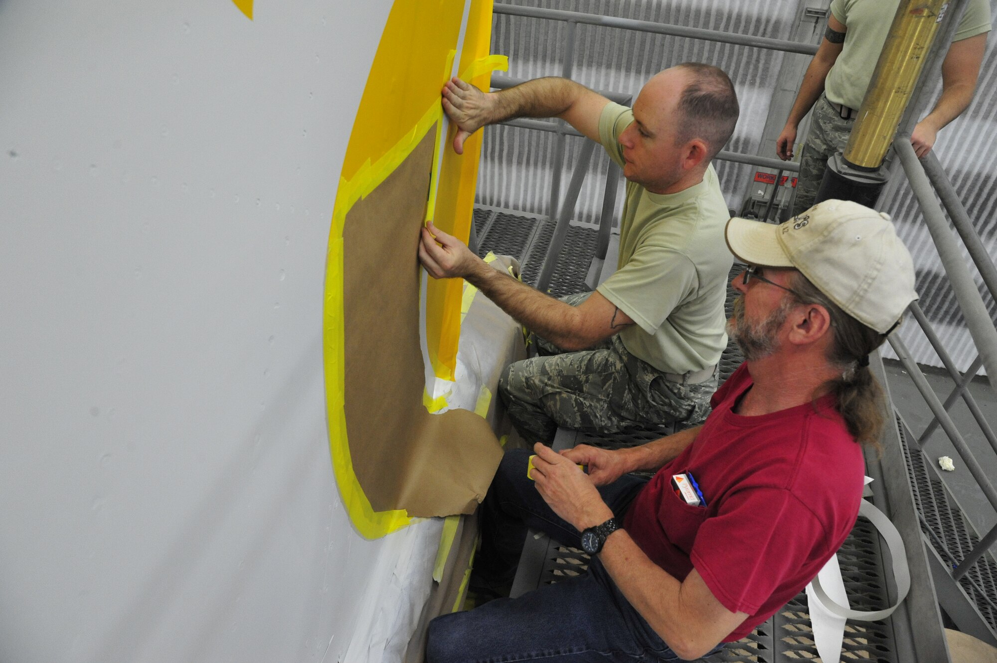 FROM LEFT: Staff Sgt. Justin Spurlock, 56th Equipment Maintenance Squadron aircraft structural maintenance craftsman, and Michael Rairden, 56th EMS aircraft painter, tape down a stencil of the Merlion design Oct. 17 in the corrosion building paint booth. The Merlion, which has a head of a lion and body of a fish, is an important symbol to Singapore. (U.S. Air Force photo/Senior Airman Grace Lee)