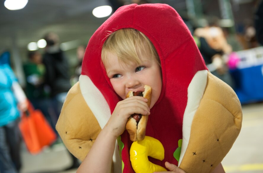 A child dressed as a hotdog takes a bite of a hotdog at the Trunk or Treat event, Oct. 31. The event, hosted by 5th Logistics Readiness Squadron Vehicle Operations and Balfour Beatty Communities, featured treats, an inflatable castle and a haunted house for base residents. (U.S. Air Force photo/Airman 1st Class Apryl Hall)