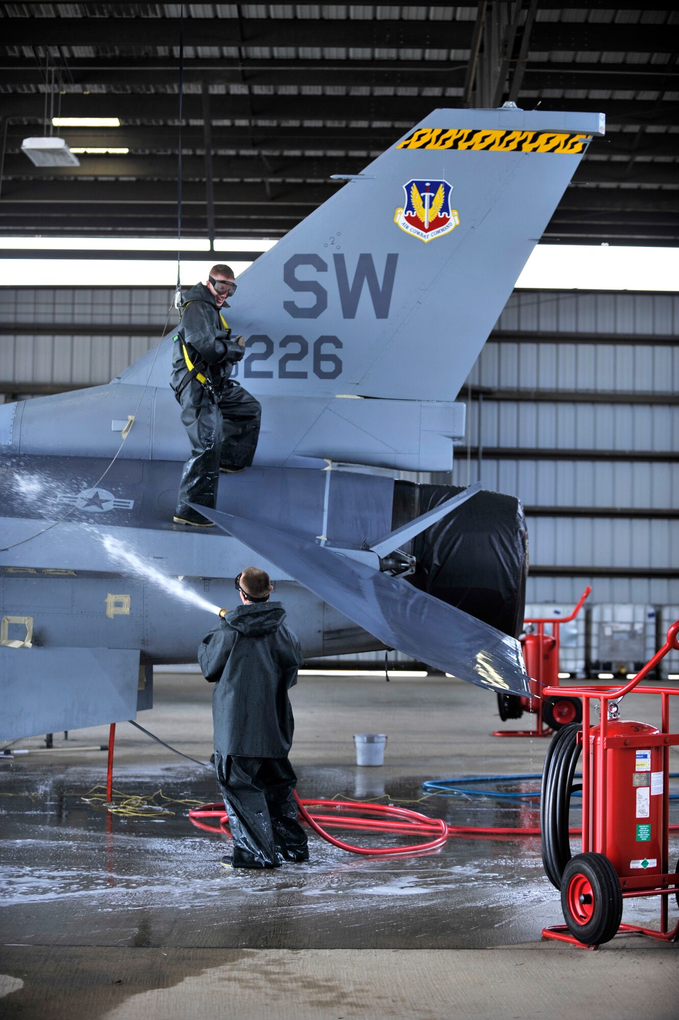 [From bottom] U.S. Air Force Senior Airman Brad Pippin, 20th Aircraft Maintenance Squadron tactical aircraft maintainer, hoses down an F-16 Fighting Falcon while Staff Sgt. Alan Dorman, 20th AMXS tactical aircraft maintainer, works above him during a routine cleaning, Shaw Air Force Base, S.C., Oct. 28, 2013. The two were part of a three-man team scrubbing the jet down from top to bottom. (U.S. Air Force photo by Airman 1st Class Jensen Stidham/Released)