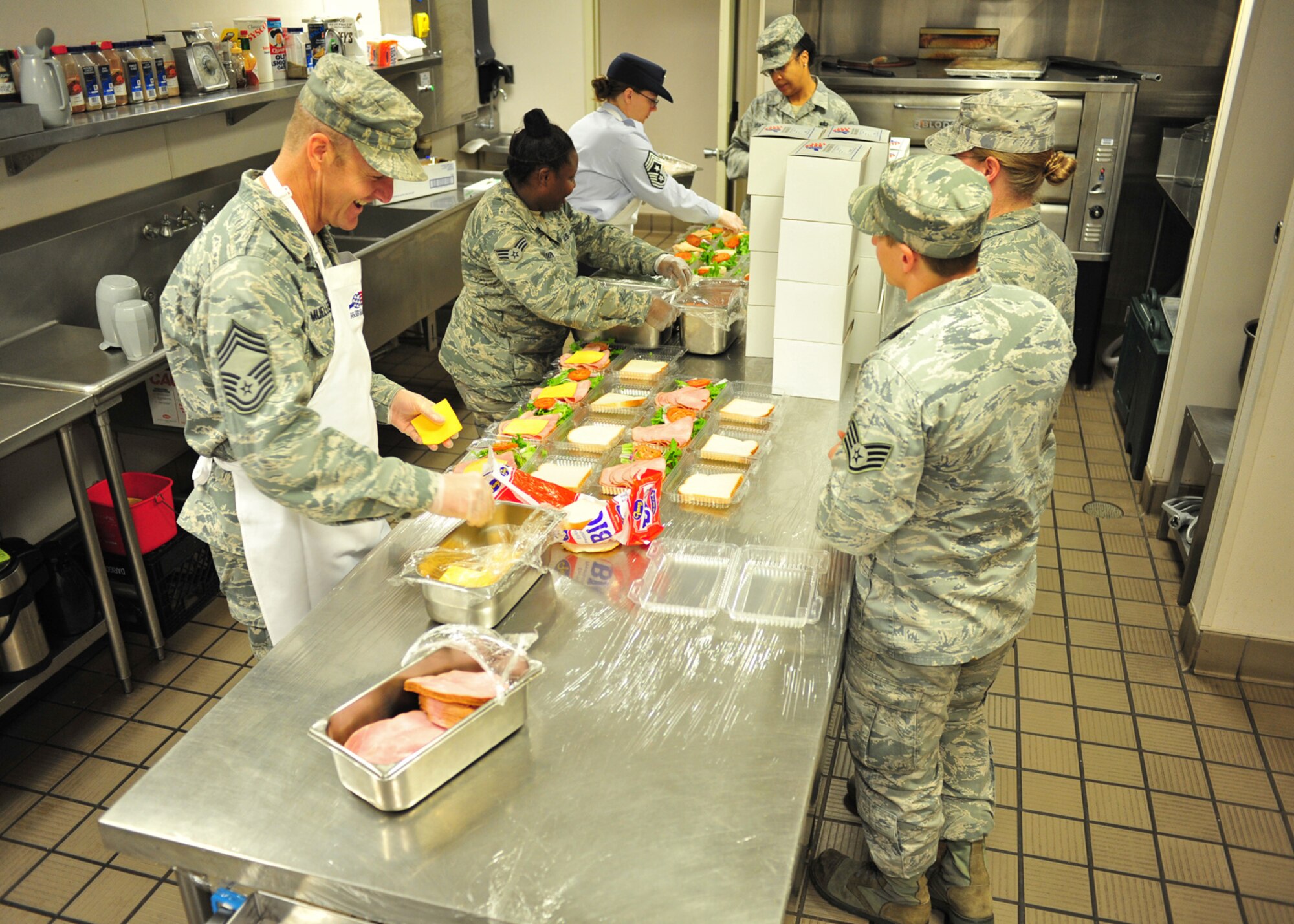 Chief Master Sgt. Wendy Hanson, 92nd Air Refueling Wing command chief, and Chief Master Sgt. Robert Mueller, 92nd Mission Support Group, assist the dining facility staff by making sandwiches for boxed lunches at Fairchild Air Force Base, Wash., Oct. 31, 2013. The boxed lunches are prepared for flyers, security forces and maintenance workers that don’t normally have enough time to stop for a meal. (U.S. Air Force photo by Senior Airman Taylor Curry/Released)