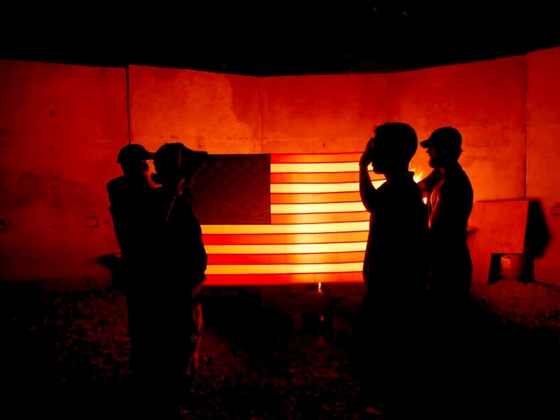 Air Force Office of Special Investigations agents conduct a reenlistment ceremony recently at an undisclosed location in Southwest Asia. A small bonfire illuminates the American flag. (U.S. Air Force Photo)