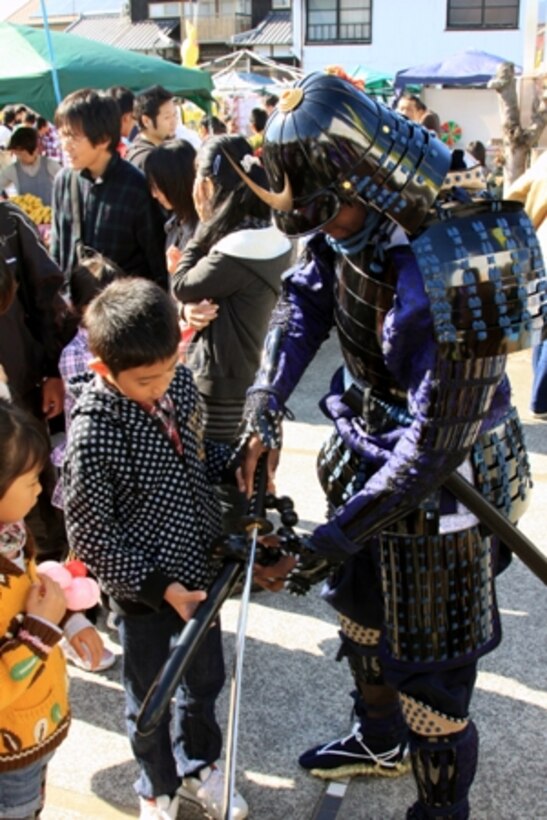Lance Cpl. Julias Hall, volunteer samurai, exchanges his kitana for a local japanese child’s balloon sword during the samurai stage performance of the 22nd Kuragake Castle Festival in Kuga, Iwakuni City, Nov. 20. Event coordinators and local volunteers appreciated the Marines taking time out of their weekend to help reflect on such an important part of the local history.