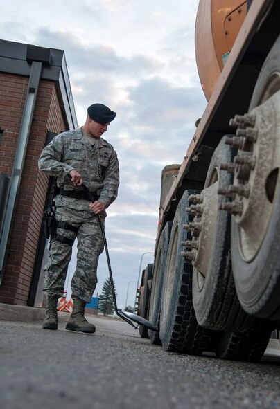Airman 1st Class Tanner Mansuetti, 5 5th Security Forces Squadron installation entry controller, searches around a vehicle’s wheel well during a routine security check here, Nov. 6, 2013. A team works the search pit to ensure vehicles that enter the base are safe and secure before doing so. (U.S. Air Force photo/Airman 1st Class Andrew Crawford)