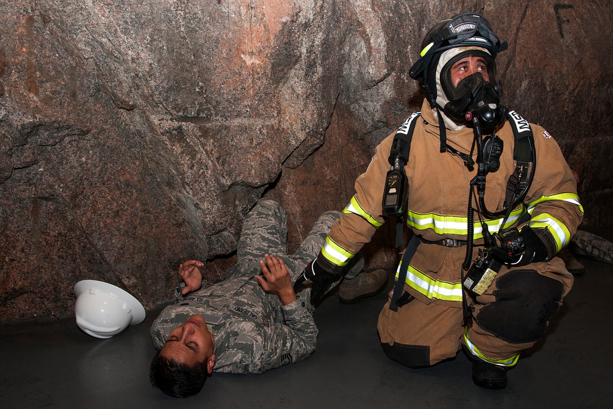 CHEYENNE MOUNTAIN AIR FORCE STATION, Colo. -- A member of the Cheyenne Mountain Air Force Station Fire Department assists Tech. Sgt. Americo Galdeano, 721st Communications Squadron, during their response to an electrical fire exercise in the Cheyenne Mountain industrial area. This realistic training was part of the Vigilant Shield exercise designed to keep Cheyenne Mountain personnel prepared for a real-world incident. (U.S. Air Force photo/Craig Denton)