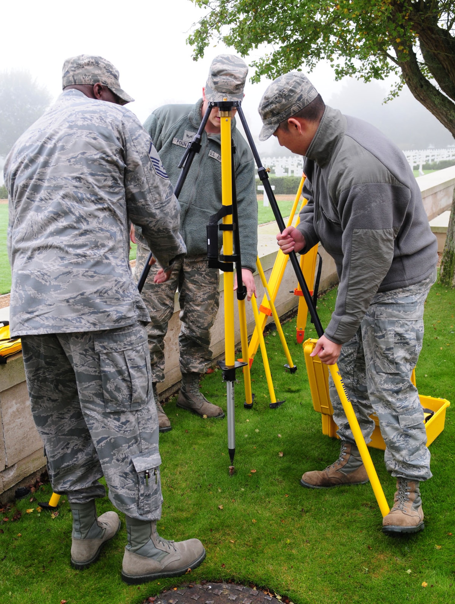 Master Sgt. Solomon Vincent, left,  assists Senior Airman Logan Fountaine, center, and Senior Airman Young Park, as they set up a quadpod ready to attach an antenna Oct. 16, 2013, at Madingley American Cemetery near Cambridge, England. The Airmen were taking GPS readings to annotate the exact location of each individual headstone. This equipment served as a base station, which collects data from 24 GPS satellites in orbit. All the data from the project will be made into an electronic map that allows families and friends of those lost in World War II to pinpoint the location of their resting place here.Vincent is a 100th Civil Engineer Squadron engineering flight superintendent and Fountaine and Park are 100th CES engineering flight journeyman.