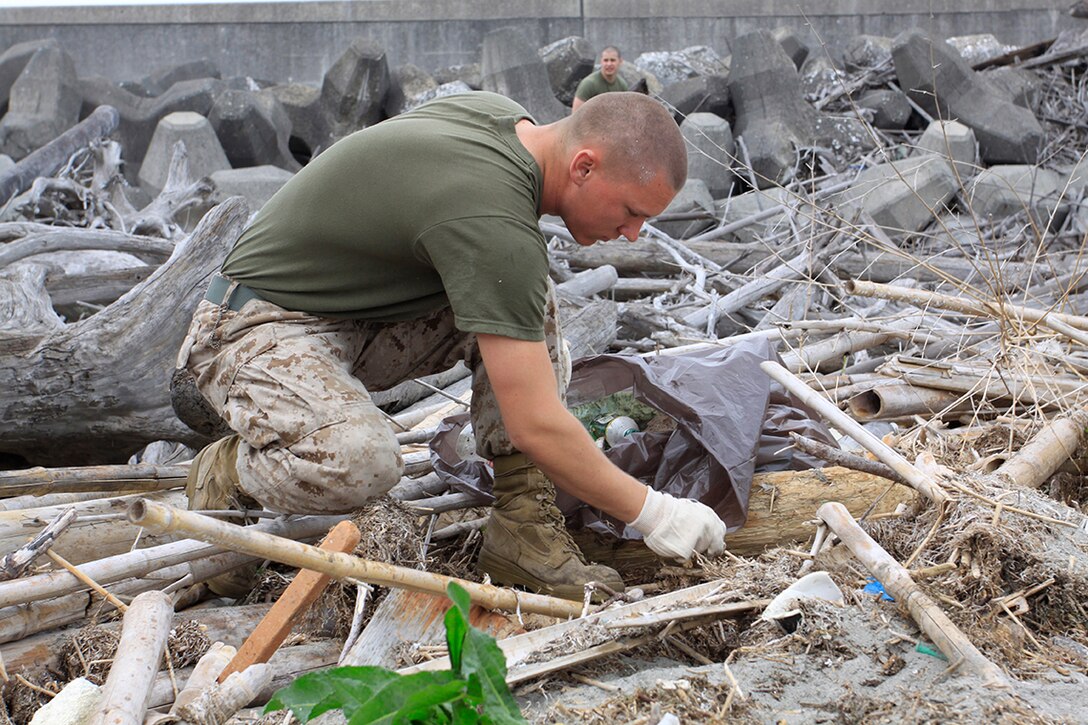 Lance Cpl. Nick Schiner, Combat Logistics Company 36 engineer equipment mechanic, gathers trash and debris along the seawall near Penny Lake during an Earth Day celebration here April 22. More than 80 Marines, sailors and station residents volunteered to clean the area around the seawall where the Nishiki River meets the Iwakuni harbor.