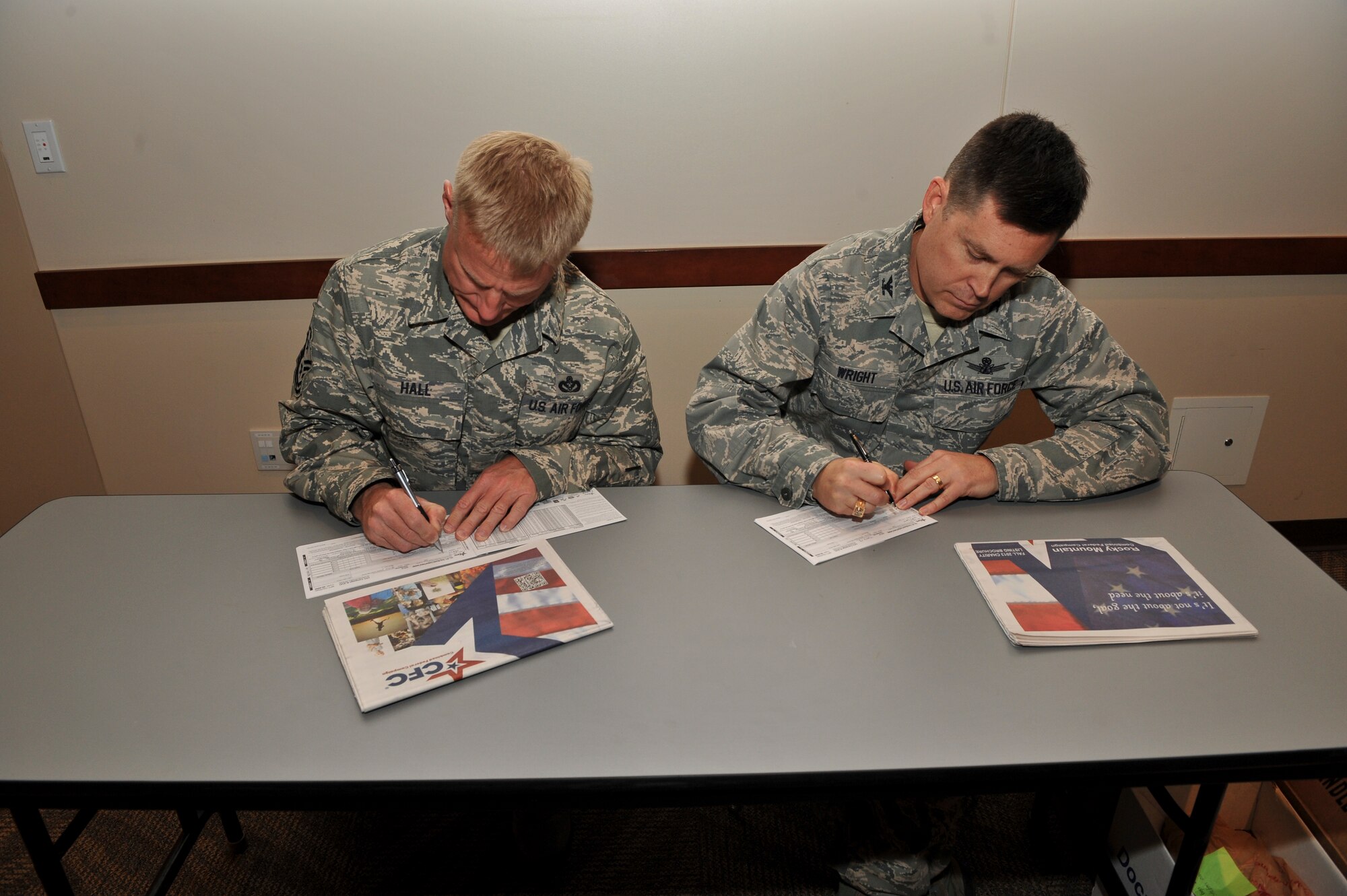 Chief Master Sgt. Craig S. Hall, 460th Space Wing command chief, left, and Col. Dan Wright, 460th SW commander, fill out their Combined Federal Campaign donation forms during the CFC kickoff event Nov. 7, 2013, at the Leadership Development Center on Buckley Air Force Base, Colo. The 2013 CFC kicked off with 55 charities being represented and donations by the wing commander and command chief. (U.S. Air Force photo by Senior Airman Phillip Houk/Released)
