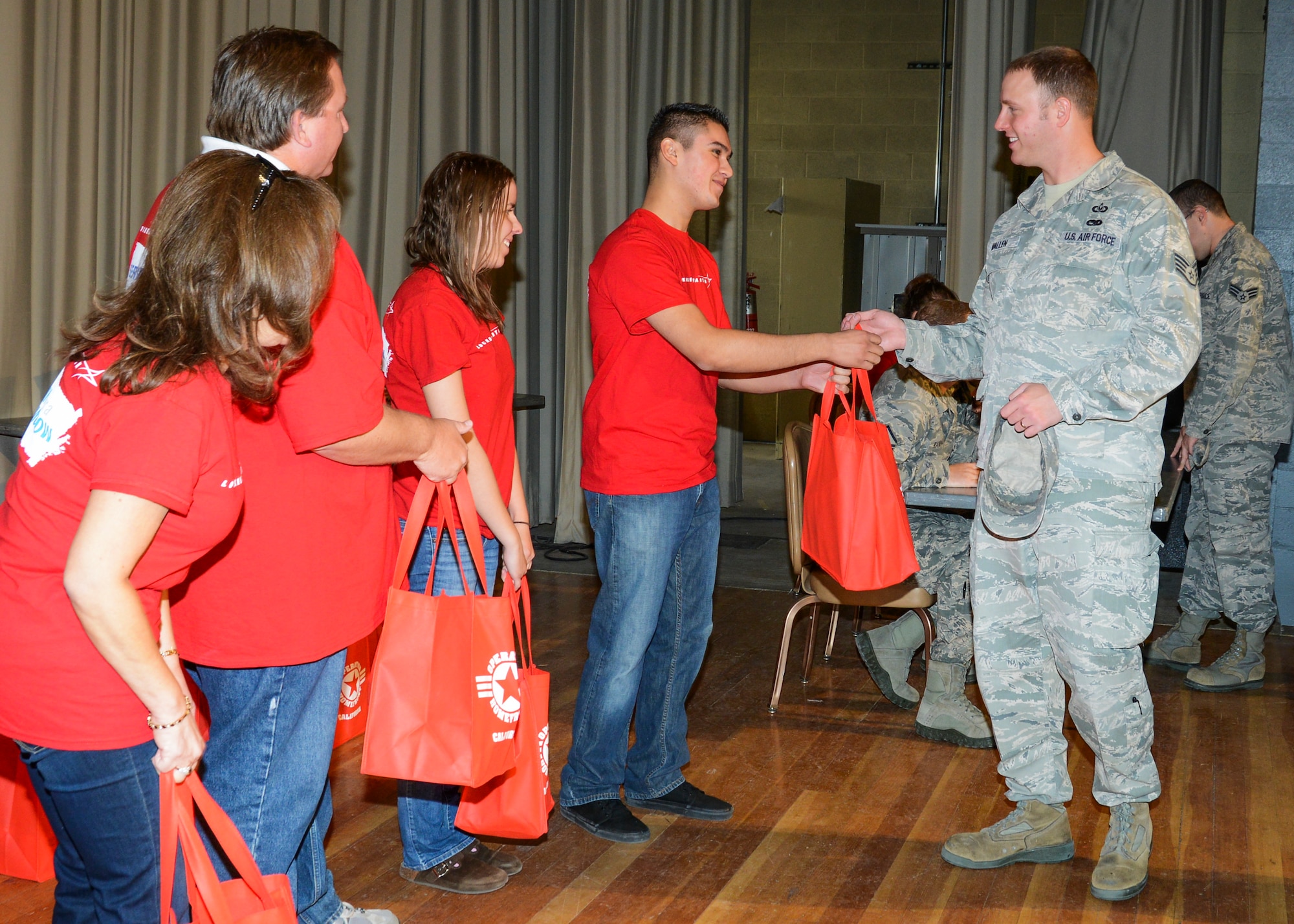 (From left to right) Lockheed Martin employees, Beatrice Aviles, Jack Danielson, Courtney Magill and Ramon Barboza Jr., handed out bags of canned foods to servicemembers in the Base Theater Nov. 7. San Diego-based Operation Homefront partnered with Lockheed Martin and the Edwards AFB First Sergeants Council to bring Thanksgiving gifts to Airmen in need. Each family received a bag of non-perishable food items and a gift card to the Commissary to purchase perishable items, like a turkey or ham, for their Thanksgiving feast. 
 (U.S. Air Force photo by Rebecca Amber)