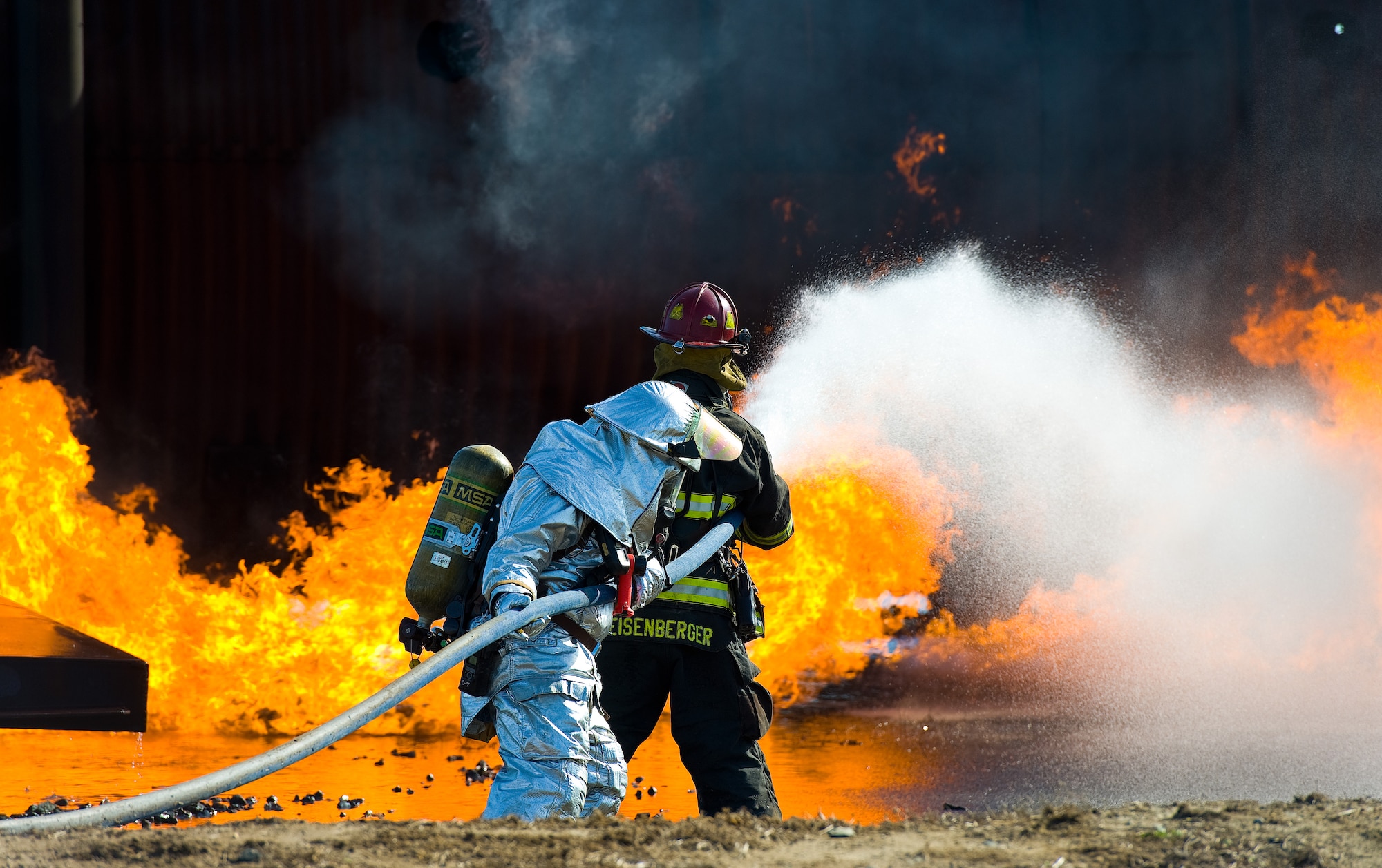 Aaron Weisenberger, back, with the 436th Civil Engineer Squadron Fire Department leads a two-person fire attack crew Nov. 4., 2013, at the fire training area on Dover Air Force Base, Del. Weisenberger sprayed water on the simulated aircraft fire using an inch and three-quarter attack line and fog nozzle. (U.S. Air Force photo/Roland Balik)