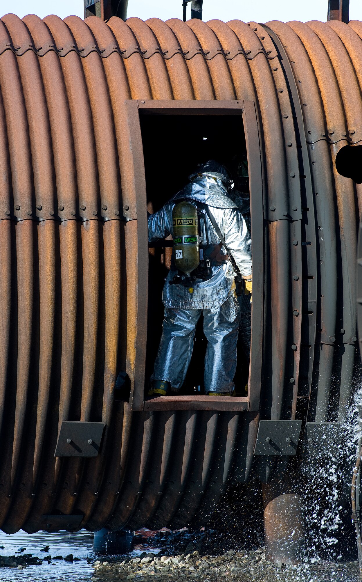 A firefighter stands inside the doorway of an aircraft fire trainer Nov. 4, 2013, at Dover Air Force Base, Del. Fire attack crews from the 436th and 512th Civil Engineer Squadrons wore aircraft rescue and firefighting proximity gear for protection when they battled a simulated aircraft fire in the cargo compartment. (U.S. Air Force photo/Roland Balik)