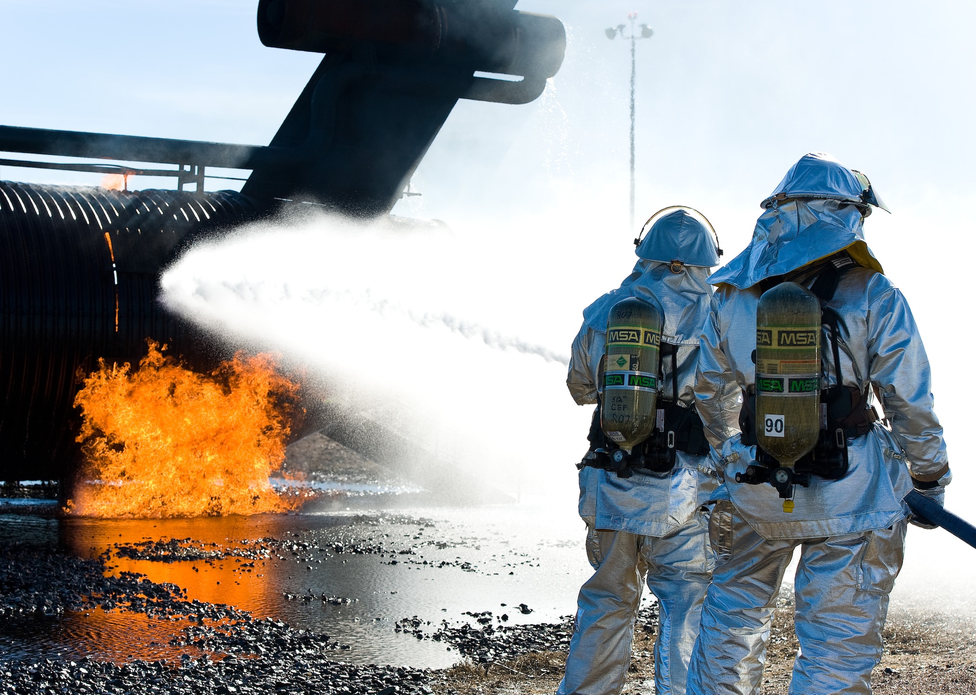 A two-person fire attack crew aims a stream of water on an aircraft fire trainer Nov. 4, 2013, at Dover Air Force Base, Del. Fire attack crews wear aircraft rescue and firefighting proximity gear for protection when battling aircraft fires. (U.S. Air Force photo/Roland Balik)