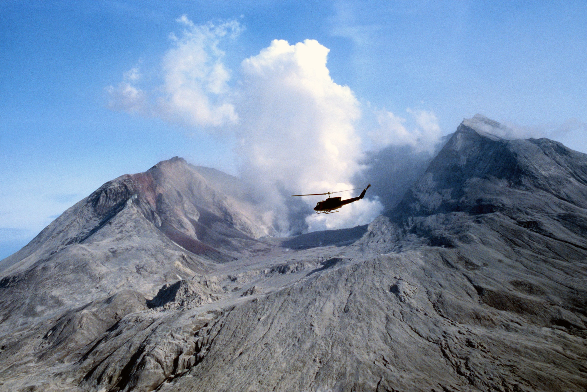 On May 18, 1980, Mount St. Helens erupted in explosion 400 times stronger than the atom bomb dropped on the Japansese city of Nagasaki 35 years earlier. The blast threw a cloud of debris 16 miles above sea level—or, roughly three times the height of Mount Everest. In the days and weeks following the eruption, the 304th Aerospace Rescue and Recovery Squadron traveled from their base at Portland International Airport, Ore., to lend a hand with humanitarian relief and any possible search-and-rescue operations. Pictured here, a UH-IN Iroquois helicopter from the 304th flies near the steam rising from the crater several days after the eruption. (U.S. Air Force photo/Master Sgt. Robert Leach)