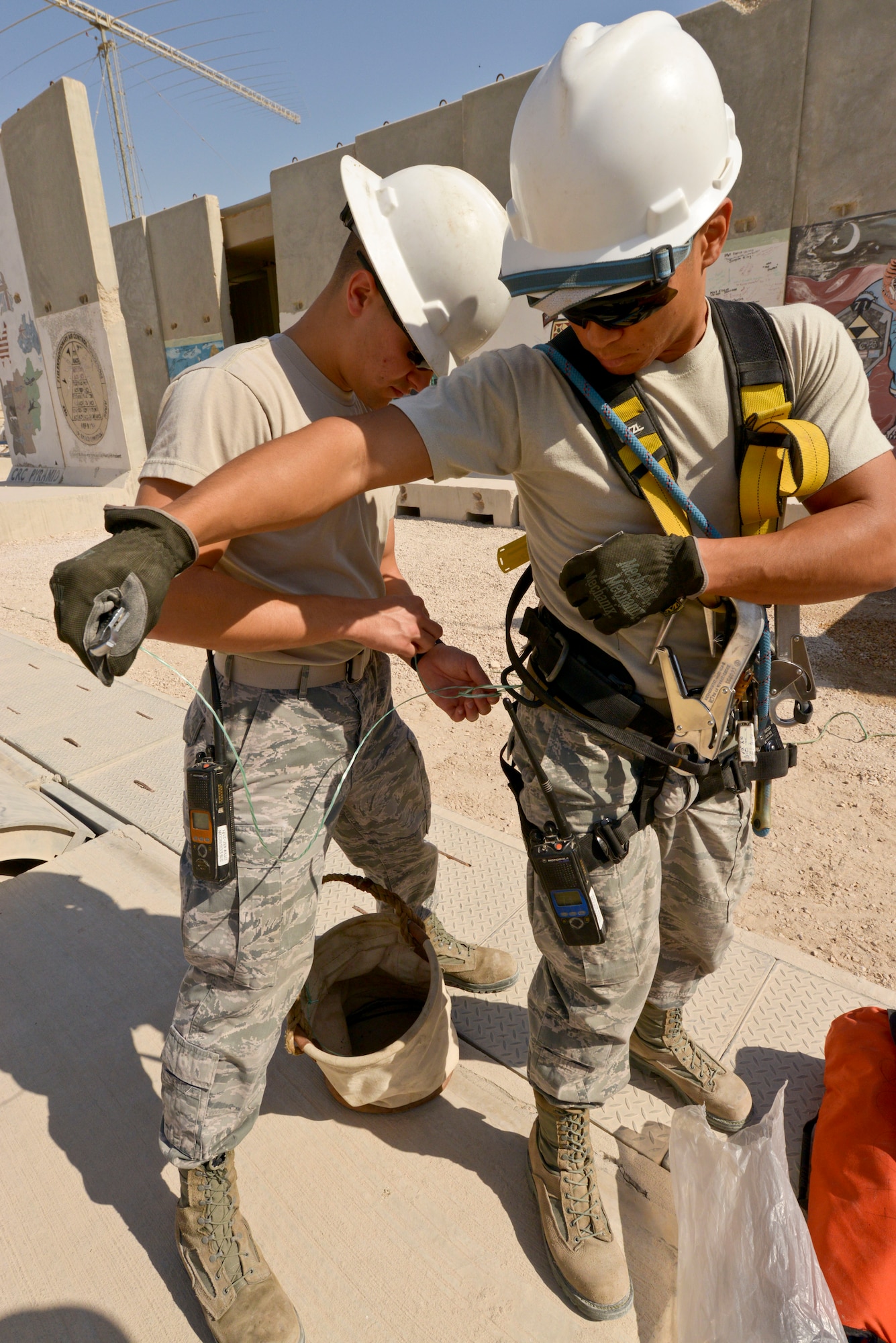 Airman 1st Class Matthew Gambal ties a knot to secure a tool to Senior Airman Wong Ly’s safety harness at the 379th Air Expeditionary Wing in Southwest Asia, Oct. 30, 2013.  Tools are secured to ensure they do not fall and injure people below during a tower climb.  Cable and antenna maintainers Gambal and Ly are with the 379th Expeditionary Communications Squadron. Gambal is deployed from Barksdale Air Force Base,La., and hails from Caledonia, Miss., and Ly is deployed from Kadena Air Base Japan and a native of Hilo, Hawaii. (U.S. Air Force photo/Tech. Sgt. Joselito Aribuabo)
