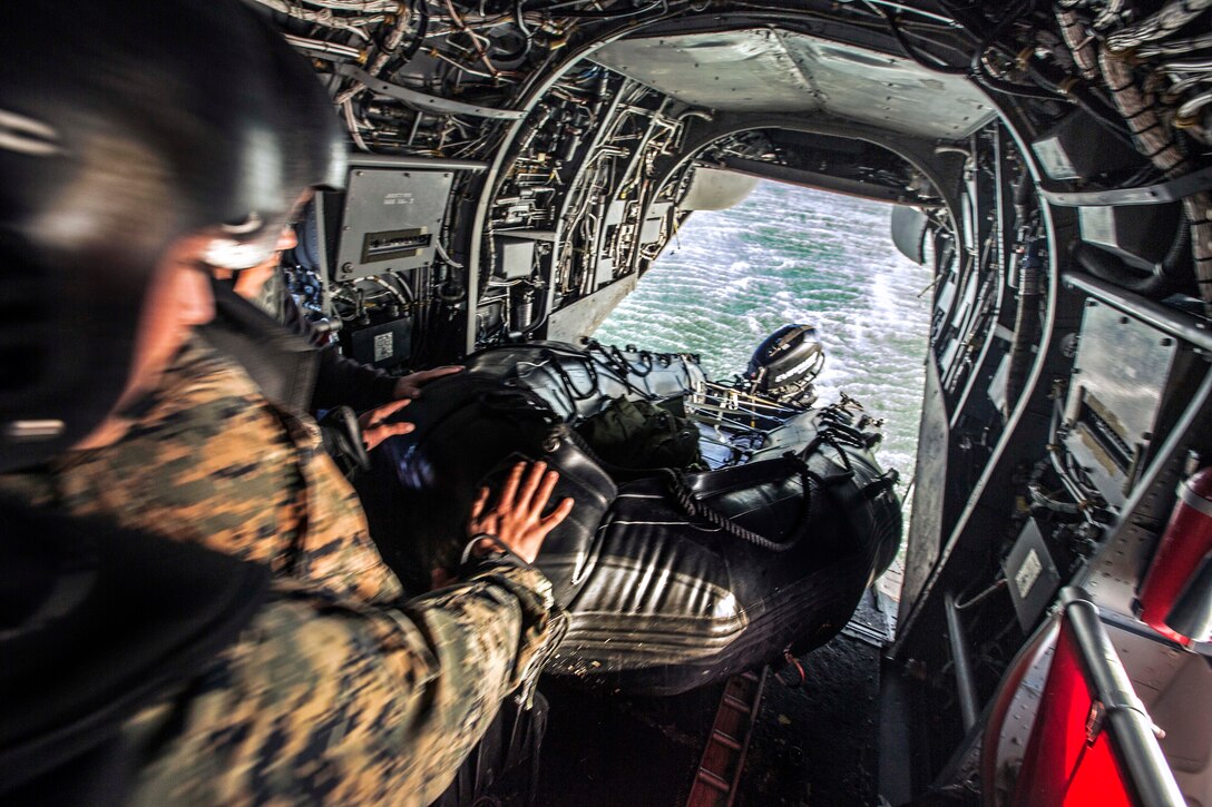 Marines and sailors push a zodiac boat out the back of a CH-46 Sea ...