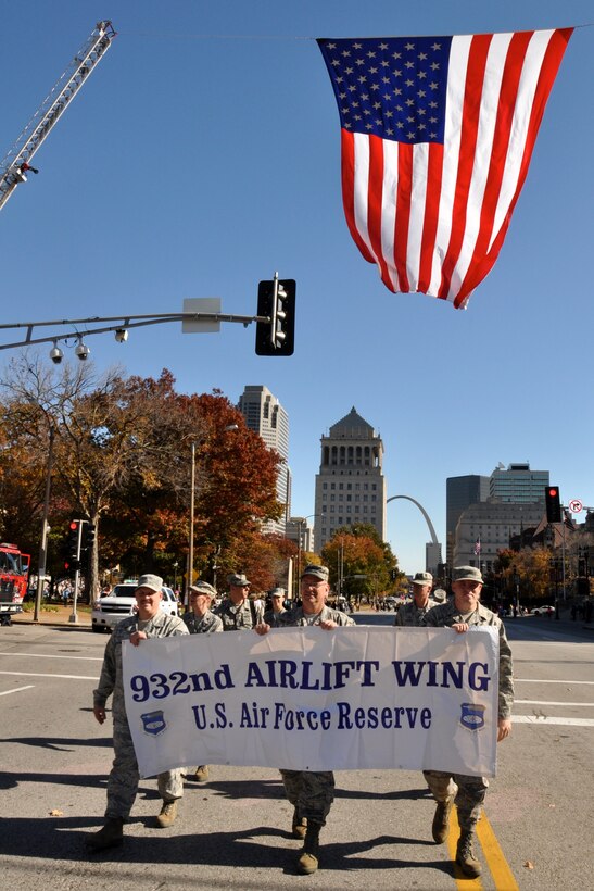 Members of the 932nd Airlift Wing march under a static display of the American flag, while smiling and waving to the crowd during the St. Louis Veterans Day parade, November 9th, 2013 in St. Louis, Mo.  (U.S. Air Force Photo by Staff Sgt. Amber Hodges)
