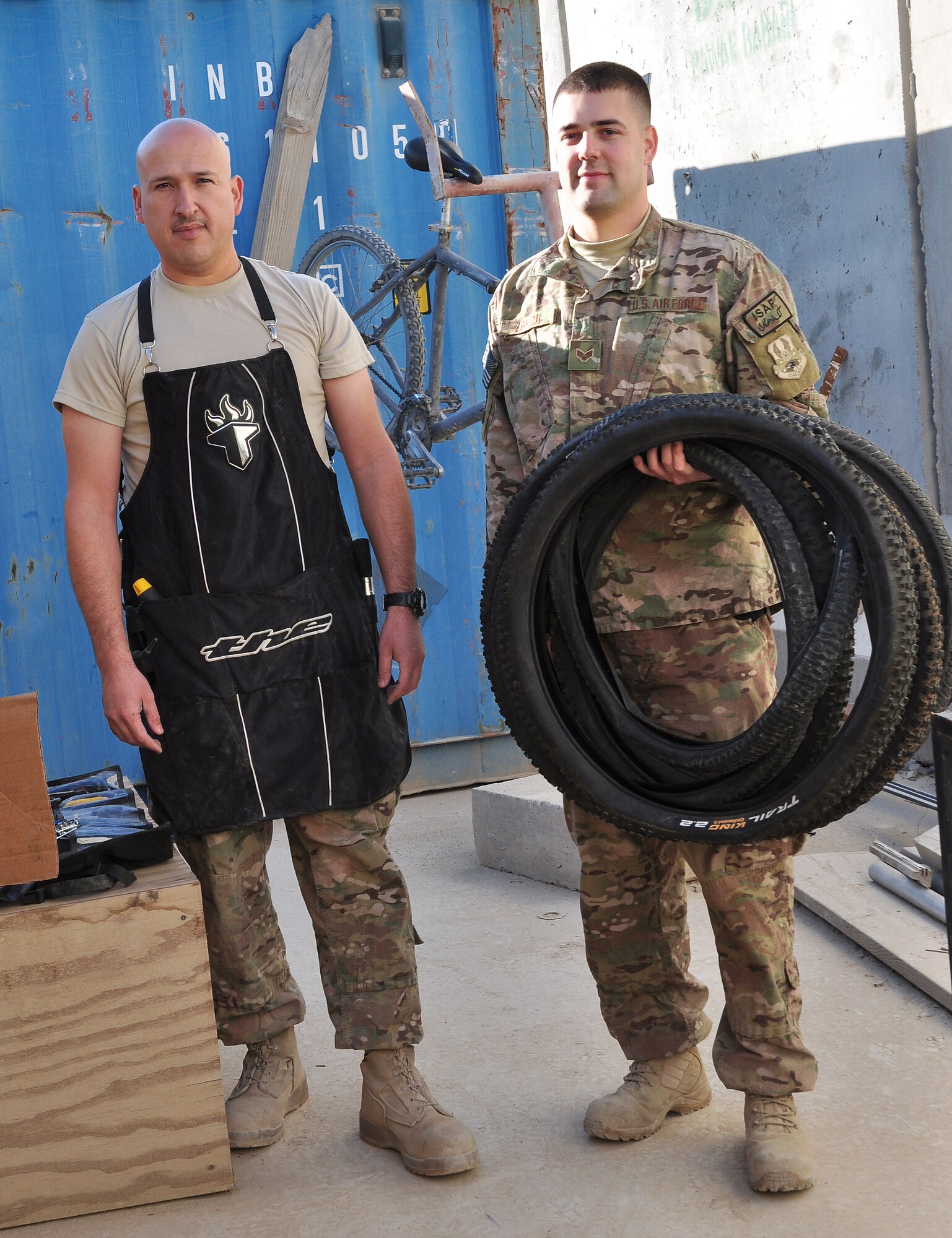 Tech. Sgt. Juan Sanchezduarte (left) and Senior Airman Mark Zorich (right), both assigned to the 451st Expeditionary Logistics Readiness Squadron, pose with some bicycle tires outside Tan Box Bike Repair at Camp Losano, Kandahar Airfield, Afghanistan, Nov. 11, 2013. Both Airmen volunteer their time and resources so service members at KAF can have free bicycle repairs available. (U.S. Air Force photo by Capt. Jason Smith)