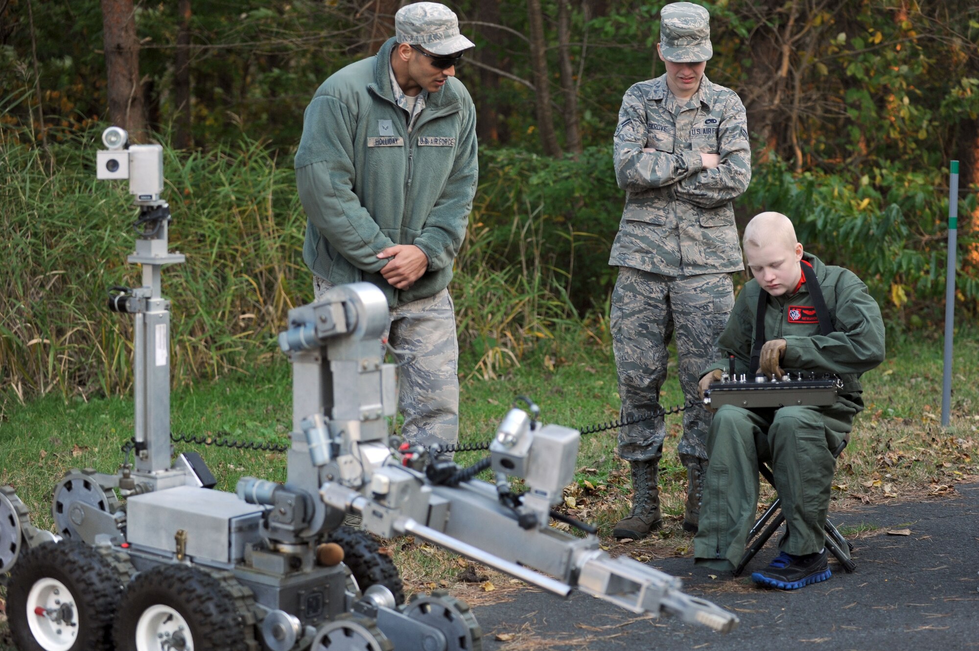 Senior Airman William Holliday, 35th Civil Engineer Squadron explosive ordnance disposal technician, and Airman 1st Class Jared Skrove, 13th Aircraft Maintenance Unit electrical and environmental maintenance specialist, watch Skrove’s 17-year-old brother, Jonah, maneuver a F6A robotics platform at Misawa Air Base, Japan, Nov. 6, 2013. The brothers were reunited thanks to the Make-A-Wish Foundation, which granted Jonah’s wish to visit his brother here. Jonah was diagnosed with osteosarcoma last fall, and lost part of his right leg in his battle with the cancer. (U.S. Air Force photo by Staff Sgt. Alyssa C. Wallace/released)