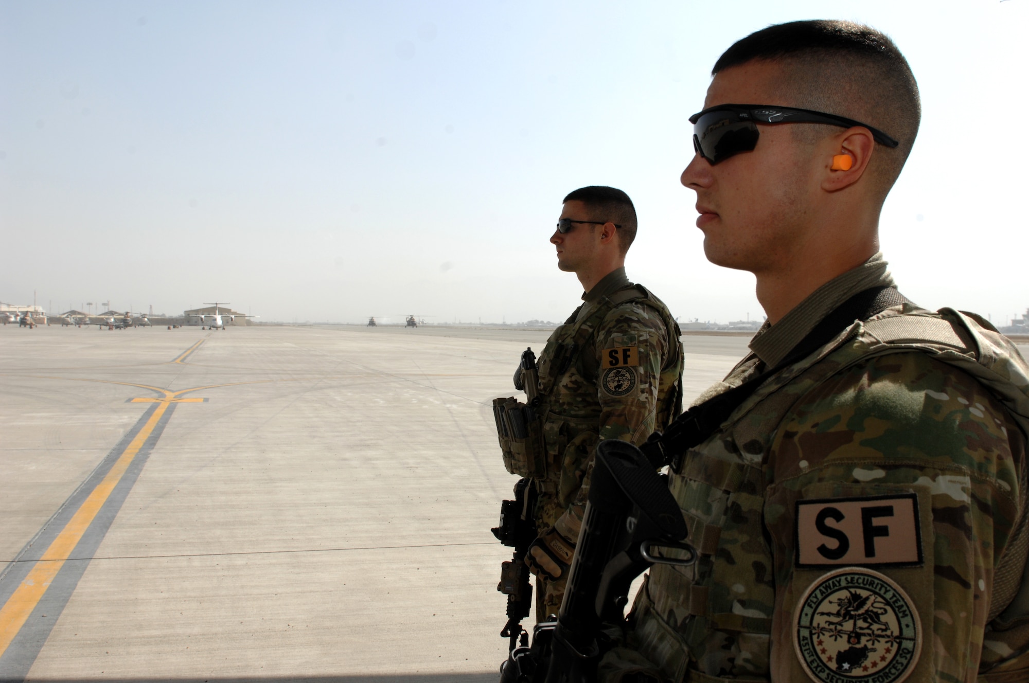 Senior Airman Alex Corderio (back), and Senior Airman James Angiola (front), look on as passengers prepare to board a C-130J Hercules at Kabul Airfield, Afghanistan, Oct. 26, 2013. Both Airmen are assigned to the 451st Expeditionary Security Forces Squadron Fly Away Security Team. FAST members provide security for the aircraft, crews and passengers as they fly to different locations, in Southwest Asia. (U.S. Air Force photo by Senior Airman Jack Sanders)