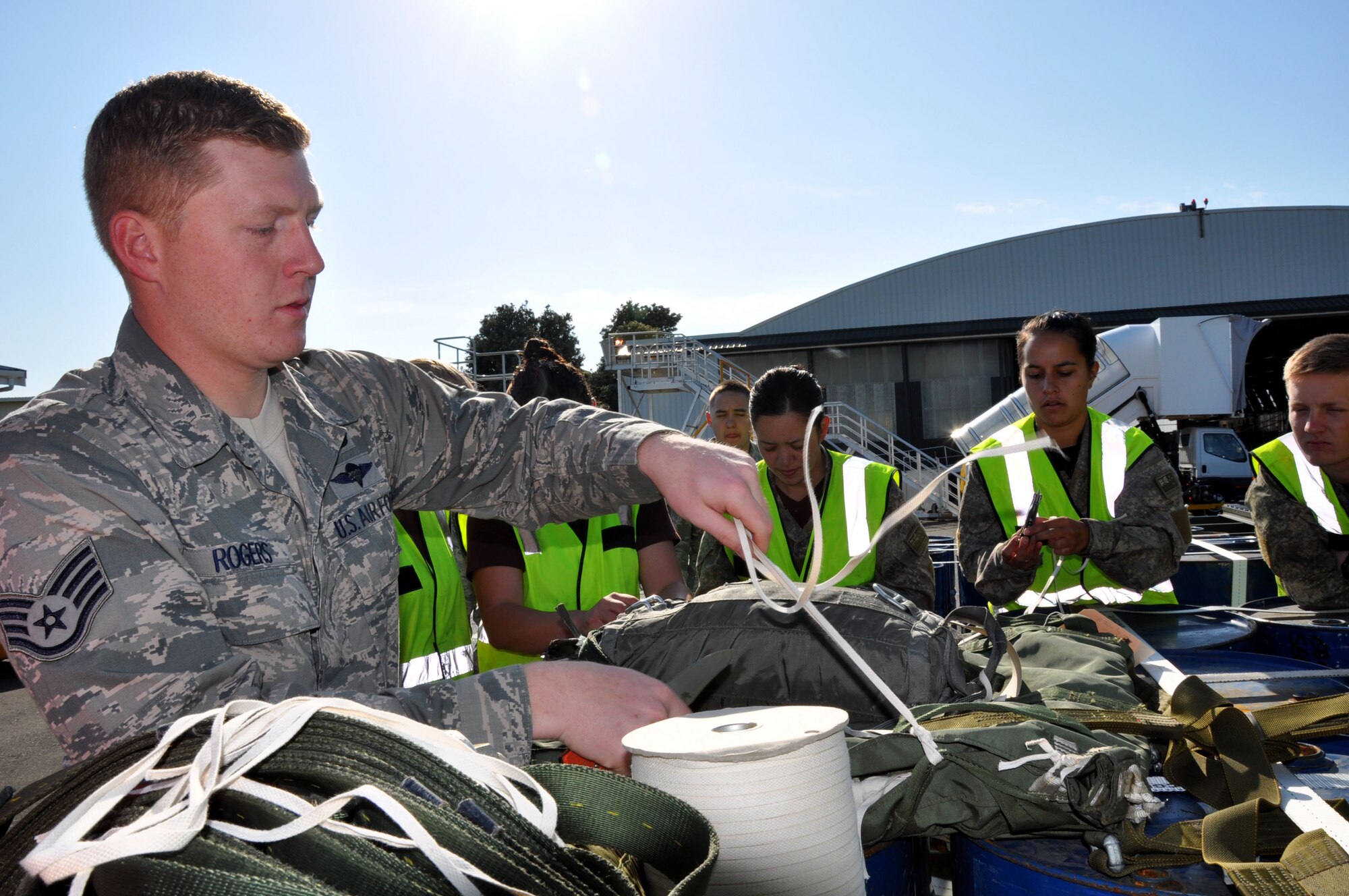 U.S. Air Force Staff Sgt. Bryan Rogers, 517th Expeditionary Airlift Squadron combat mobility specialist, weaves a length of one-quarter inch cotton webbing through a drogue parachute as military parachute riggers from three nations joined together for a subject-matter exchange at Royal New Zealand Air Force Base Ohakea, New Zealand, Nov. 11 during the second annual Exercise Kiwi Flag. U.S. Air Force trainers, deployed to the 517th Expeditionary Airlift Squadron, taught attendees how to rig a “15-foot extraction chute to the 160-foot extraction line” for cargo air drops from the C-17 Globemaster III. The small drogue chute, attached to a 60-foot line, sits in the back of the aircraft where it is pre-staged to catch the air current from the open ramp when activated mid-flight. When the drogue chute catches the current, the drogue rapidly pulls the extraction package, which in turn, pulls the cargo through the opening in the rear of the plane. The combat mobility team, deployed from the 773rd Logistics Readiness Squadron at Joint Base Elmendorf-Richardson, Alaska, trained more than 20 personnel from the New Zealand Army, the RNZAF and the Republic of Singapore Air Force. The Pacific-partners will have numerous opportunities to practice the newly-attained skill during the exercise which runs through Nov. 29. Kiwi Flag personnel are supporting Exercise Southern Katipo -- held on New Zealand’s South Island -- by managing air operations and providing cargo and passenger airlift including tactical air drops to SK participants. Rogers hails from Virginia Beach, Va. (U.S. Air Force Photo by Senior Master Sgt. Denise Johnson/Released)