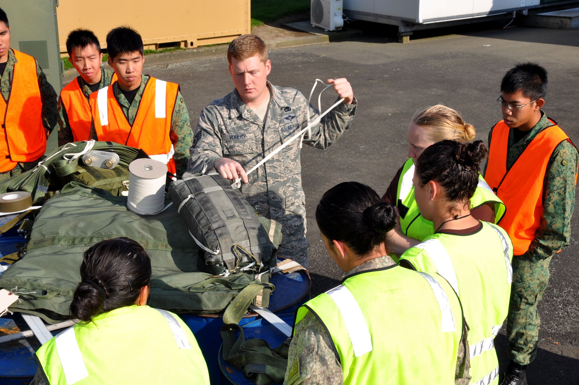 U.S. Air Force Staff Sgt. Bryan Rogers, 517th Expeditionary Airlift Squadron combat mobility specialist, weaves a length of one-quarter inch cotton webbing through a drogue parachute as military parachute riggers from three nations joined together for a subject-matter exchange at Royal New Zealand Air Force Base Ohakea, New Zealand, Nov. 11 during the second annual Exercise Kiwi Flag. U.S. Air Force trainers deployed to the 517th Expeditionary Airlift Squadron taught attendees how to rig a “15-foot extraction chute to the 160-foot extraction line” for cargo air drops from the C-17 Globemaster III. The small drogue chute, attached to a 60-foot line, sits in the back of the aircraft where it is pre-staged to catch the air current from the open ramp when activated mid-flight. When the drogue chute catches the current, the drogue rapidly pulls the extraction package, which in turn, pulls the cargo through the opening in the rear of the plane. The combat mobility team, deployed from the 773rd Logistics Readiness Squadron at Joint Base Elmendorf-Richardson, Alaska, trained more than 20 personnel from the New Zealand Army, the RNZAF and the Republic of Singapore Air Force. The Pacific-partners will have numerous opportunities to practice the newly-attained skill during the exercise which runs through Nov. 29. Kiwi Flag personnel are supporting Exercise Southern Katipo -- held on New Zealand’s South Island -- by managing air operations and providing cargo and passenger airlift including tactical air drops to SK participants. Rogers hails from Virginia Beach, Va. (U.S. Air Force Photo by Senior Master Sgt. Denise Johnson/Released)