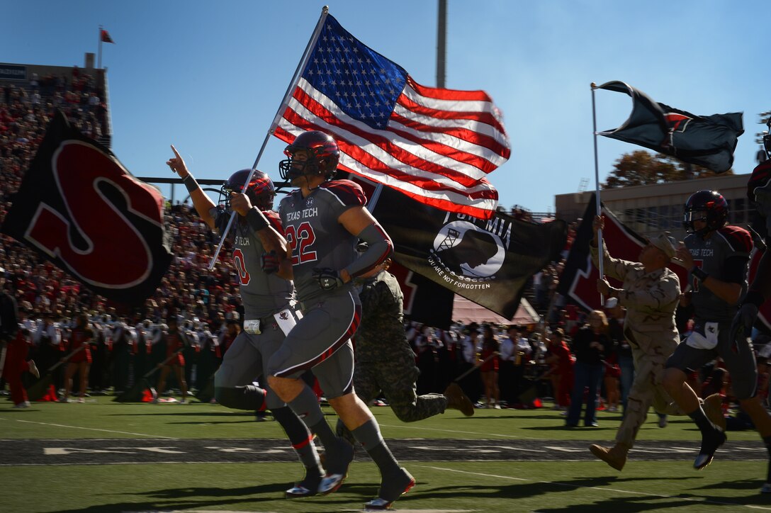 Football players display the American and Prisoner of War/Missing in Action flags as they sprint across the field prior to a game Nov. 9, 2013, in Lubbock Texas. U.S. service members were invited to attend a free football game as the Texas Tech Red Raiders took on the Kansas State Wildcats for Military Appreciation Day. (U.S. Air Force photo/Staff Sgt. Matthew Plew)