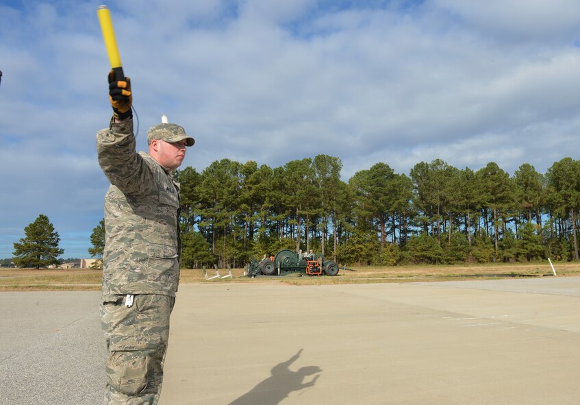 U.S. Air Force Senior Airman Christopher Paillot, 20th Civil Engineering Squadron fire fighter, signals another fire department Airman to rewind the cable using the mobile aircraft arresting system , Shaw Air Force Base, S.C., Nov 6, 2013. During a real world in-flight emergency, the fire department personnel are responsible for resetting the MAAS in case of future IEFs. (U.S. Air Force photo by Senior Airman Tabatha Zarrella/Released)

