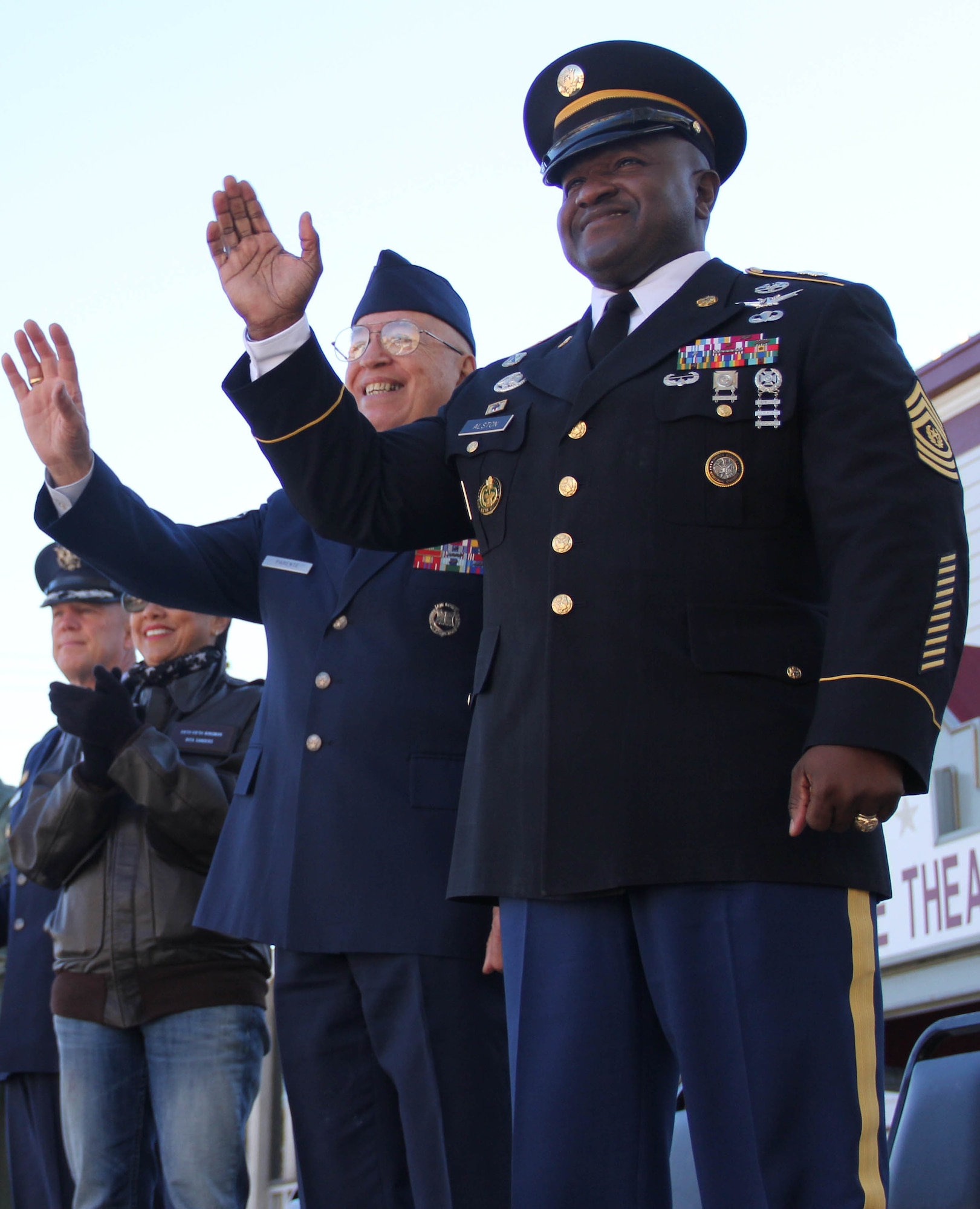 U.S. Army Command Sgt. Maj. Patrick Alston, U.S. Strategic Command senior enlisted advisor, and retired U.S. Air Force Chief Master Sgt. Michael Parente, parade grand marshal, wave to participants as pass the reviewing stand during the 14th annual Veterans Day Parade in Olde Towne Bellevue, Neb., Nov. 9. The 55th Wing, U.S. Strategic Command and Air Force Weather Agency joined with the members from the community to honor veterans at this annual parade. (U.S. Air Force photo by 2nd Lt. Carly A. Costello/Released)