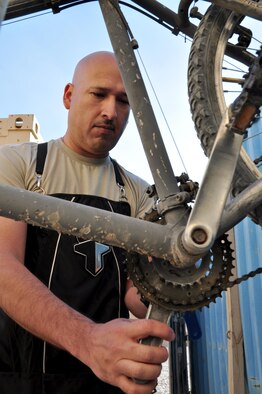 Tech. Sgt. Juan Sanchezduarte works on a bicycle at Tan Box Bike Repair Nov. 11, 2013, at Camp Losano, Kandahar Airfield, Afghanistan. Sanchezduarte volunteers his time to give service members at KAF free bicycle repairs. Sanchezduarte is a member of the 451st Expeditionary Logistics Readiness Squadron.