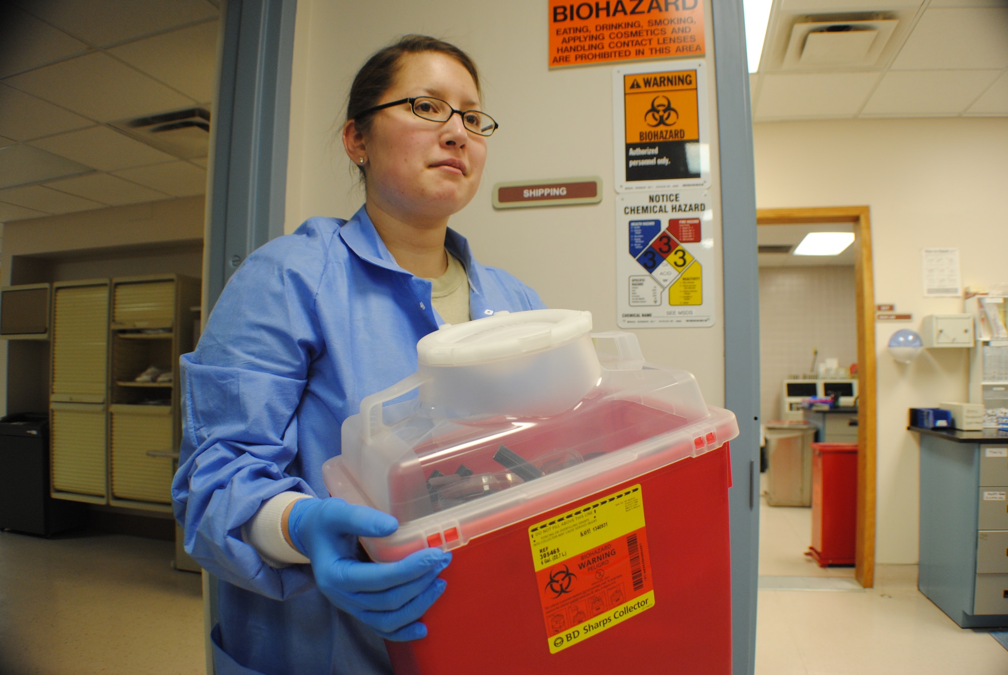Senior Airman Katherine Herzer, 319th Medical Support Squadron laboratory technician, removes a biohazard bin to properly seal it for shipment to an incinerator Nov. 8, 2013, at the medical laboratory on Grand Forks Air Force Base, N.D. The base medical laboratory complies with federal regulations and laws for medical sample handling by using warning labels such as the biohazard symbol and requiring all authorized lab technicians wear latex gloves. (U.S. Air Force photo/Staff Sgt. Luis Loza Gutierrez)